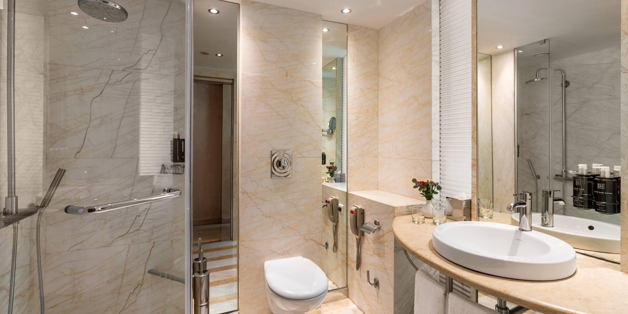Modern hotel bathroom with marble walls, glass shower, toilet, and vanity sink.