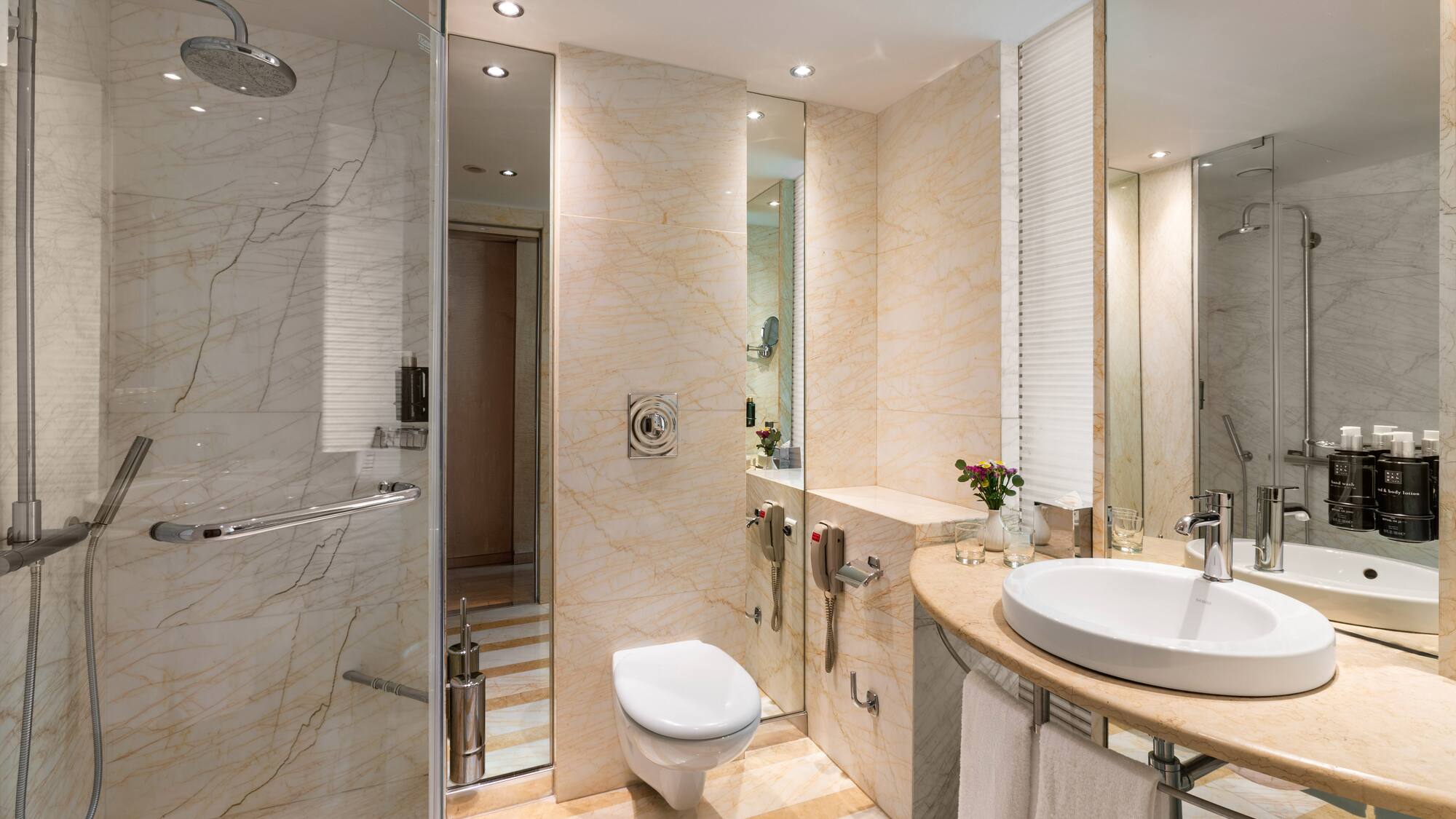 Modern hotel bathroom with marble walls, glass shower, toilet, and vanity sink.