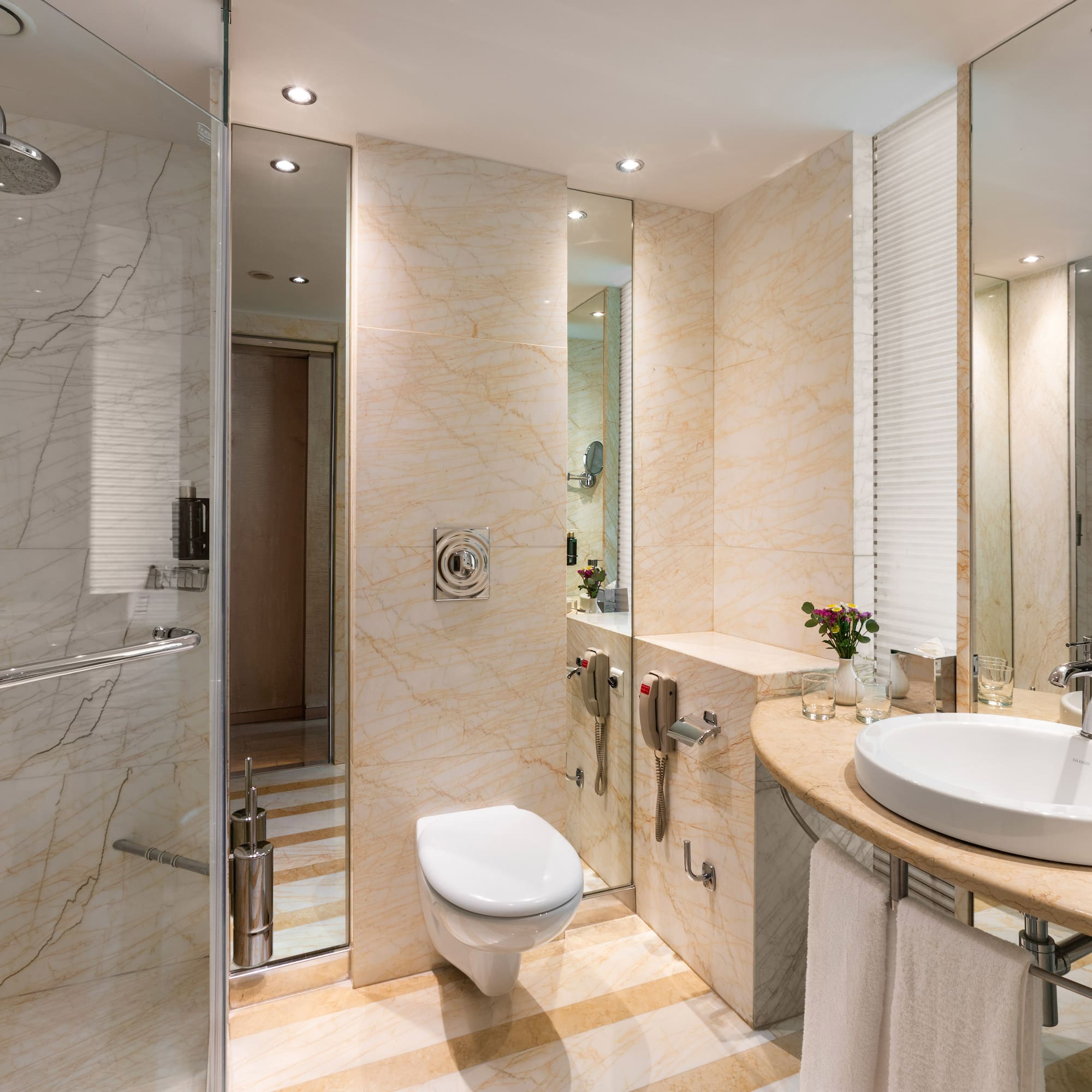 Modern hotel bathroom with marble walls, glass shower, toilet, and vanity sink.