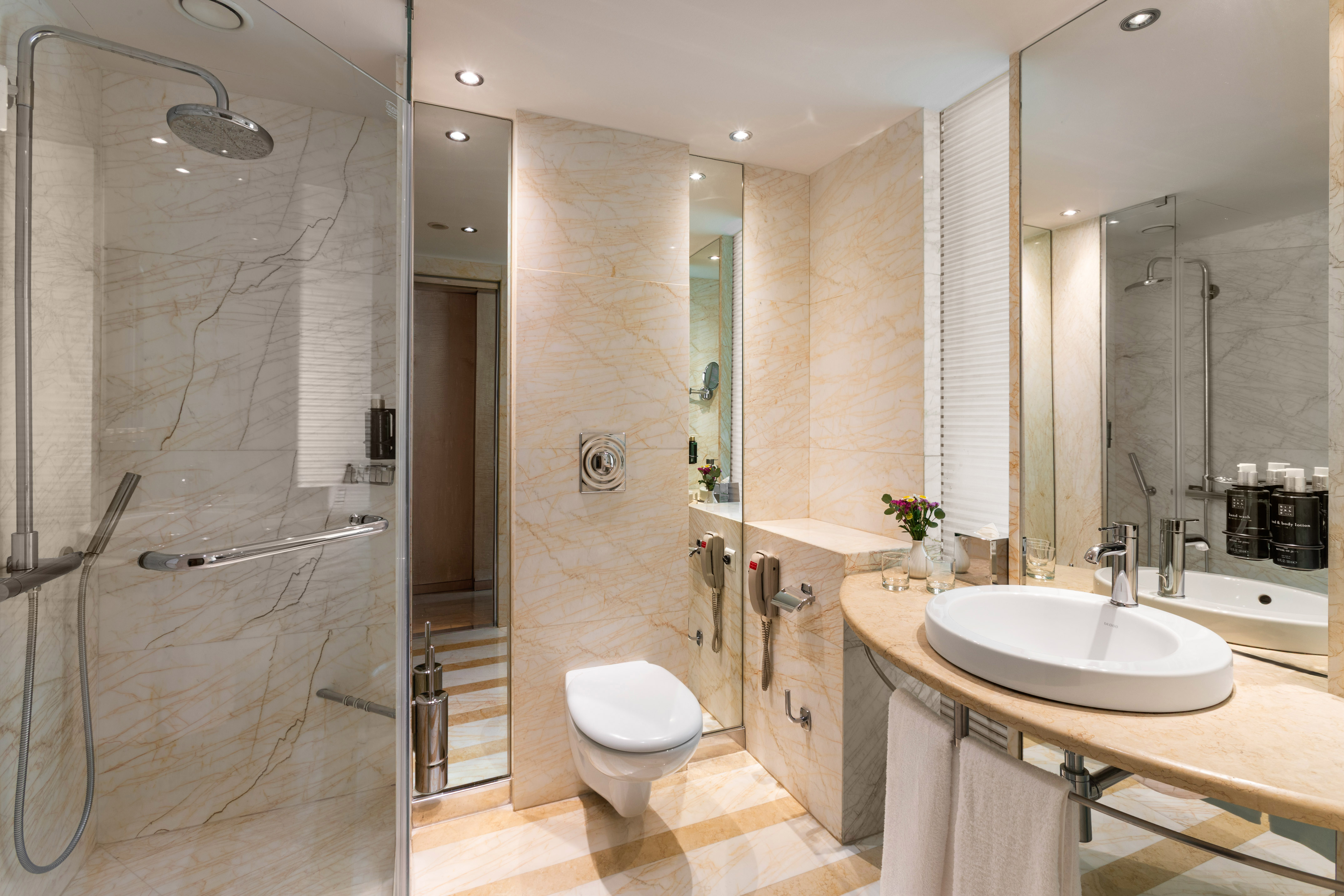 Modern hotel bathroom with marble walls, glass shower, toilet, and vanity sink.