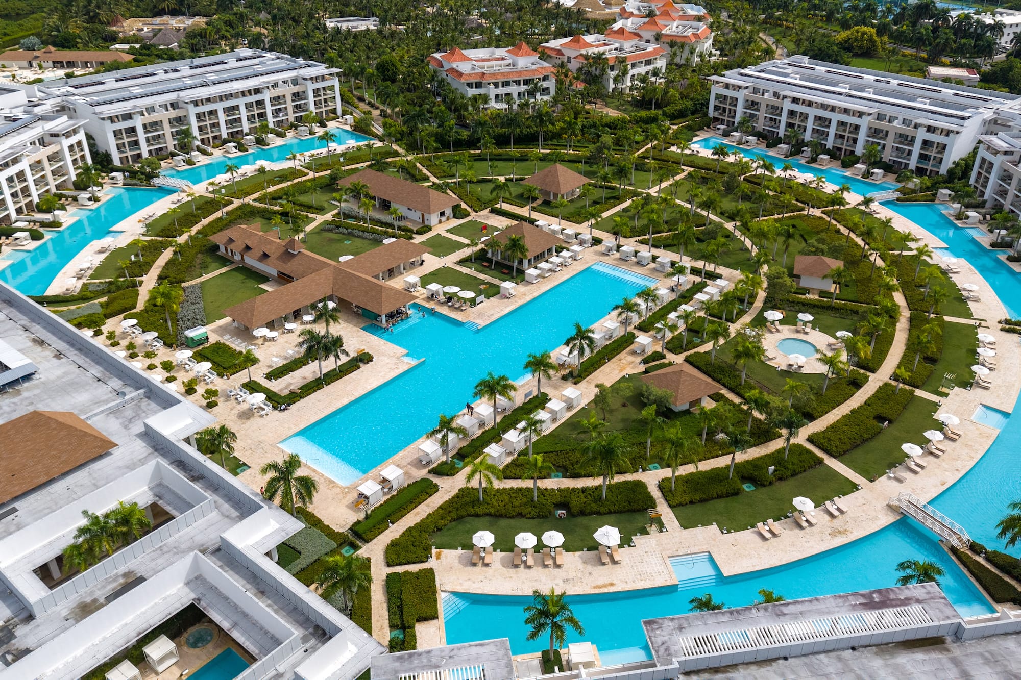 Tropical resort aerial: sprawling blue pools, palm trees, and modern buildings.