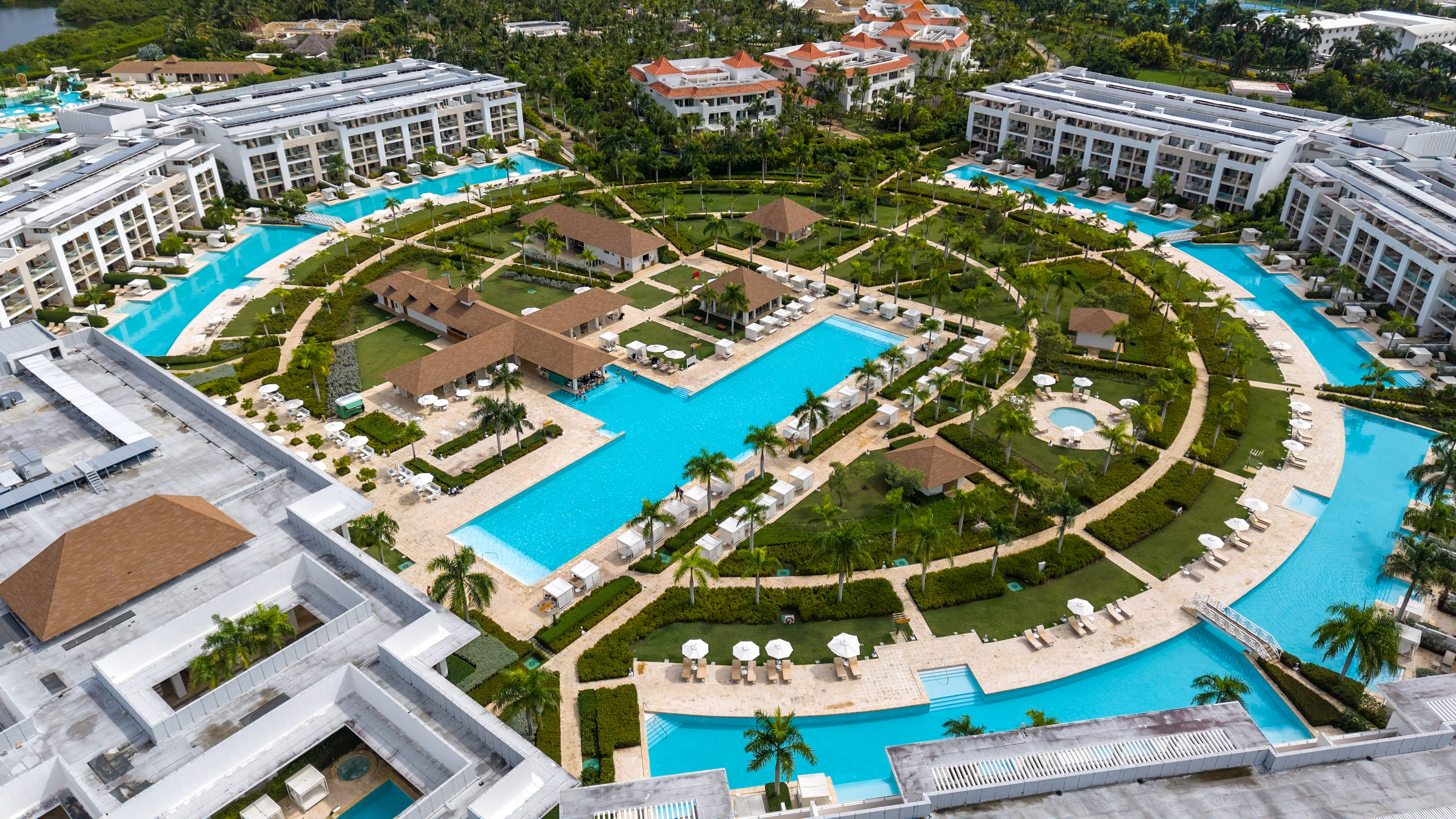 Tropical resort aerial: sprawling blue pools, palm trees, and modern buildings.