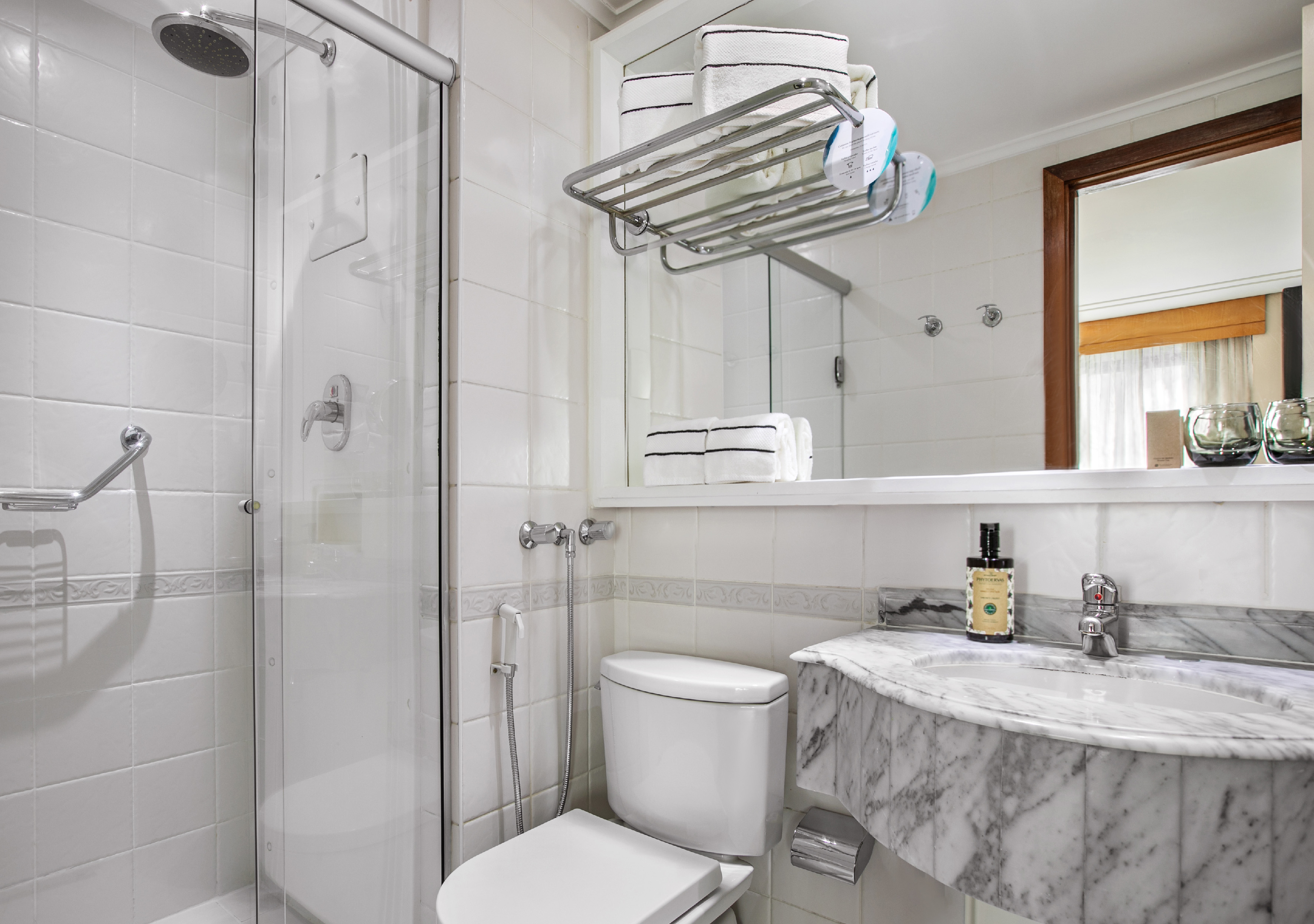 Clean white bathroom with glass shower, toilet, marble vanity, and towels.