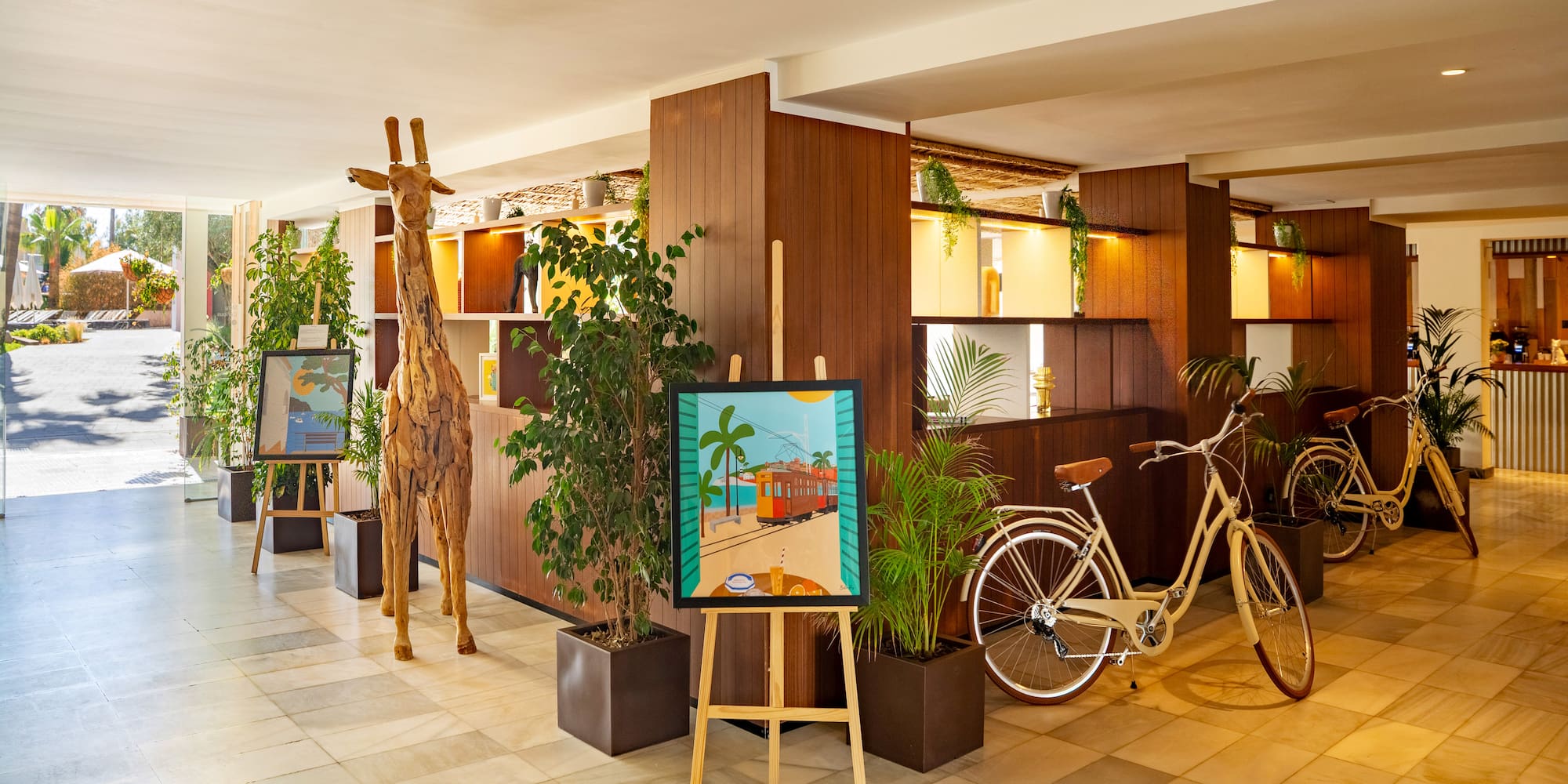 Modern hotel lobby with tropical decor, wooden giraffe, art, and vintage bicycles.