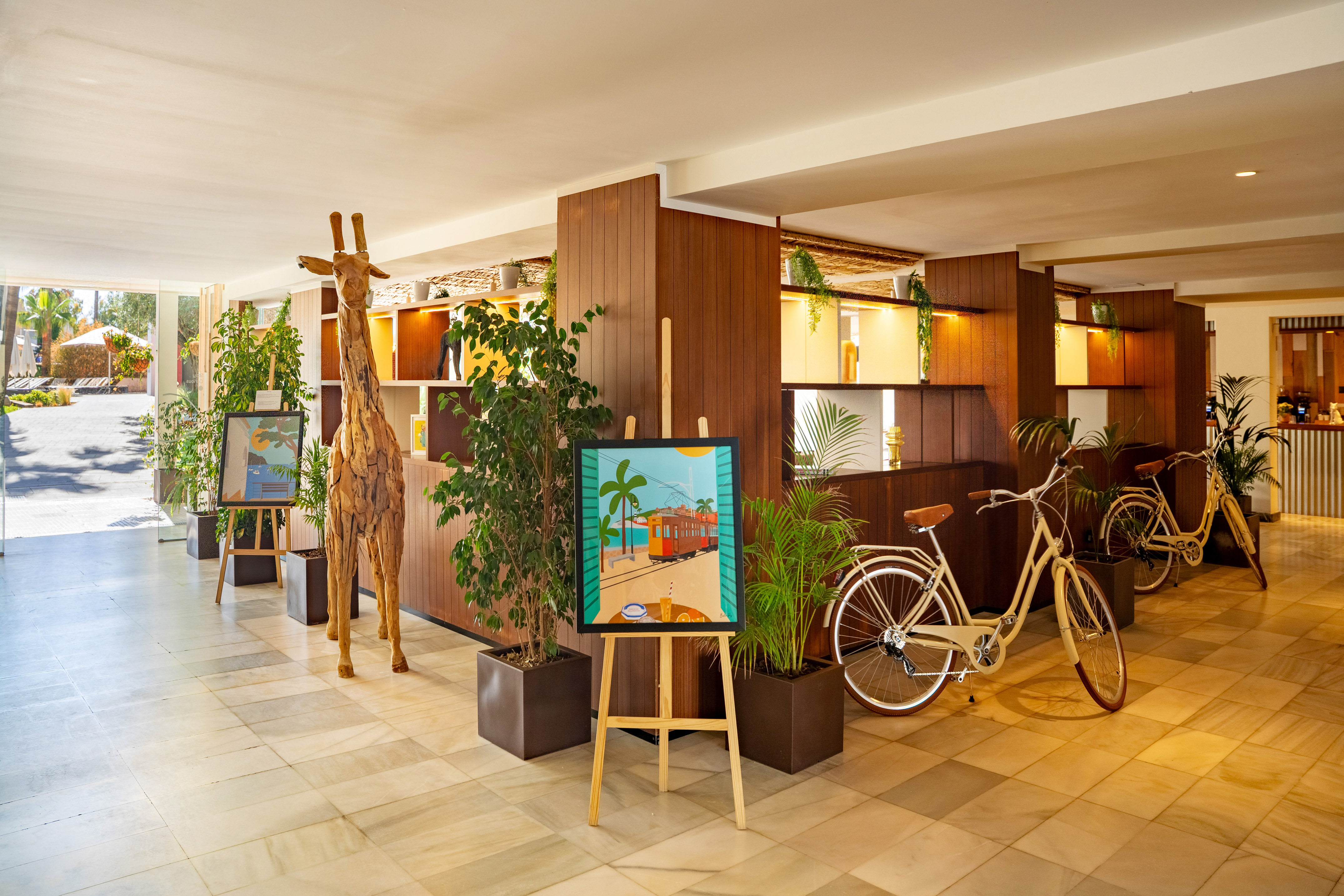 Modern hotel lobby with tropical decor, wooden giraffe, art, and vintage bicycles.