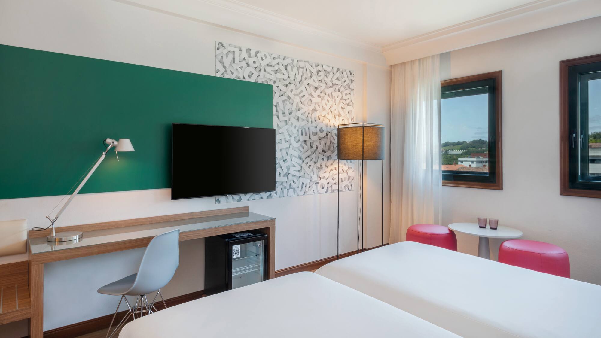 Modern hotel guest room with twin beds, desk, TV, and unique wall art.