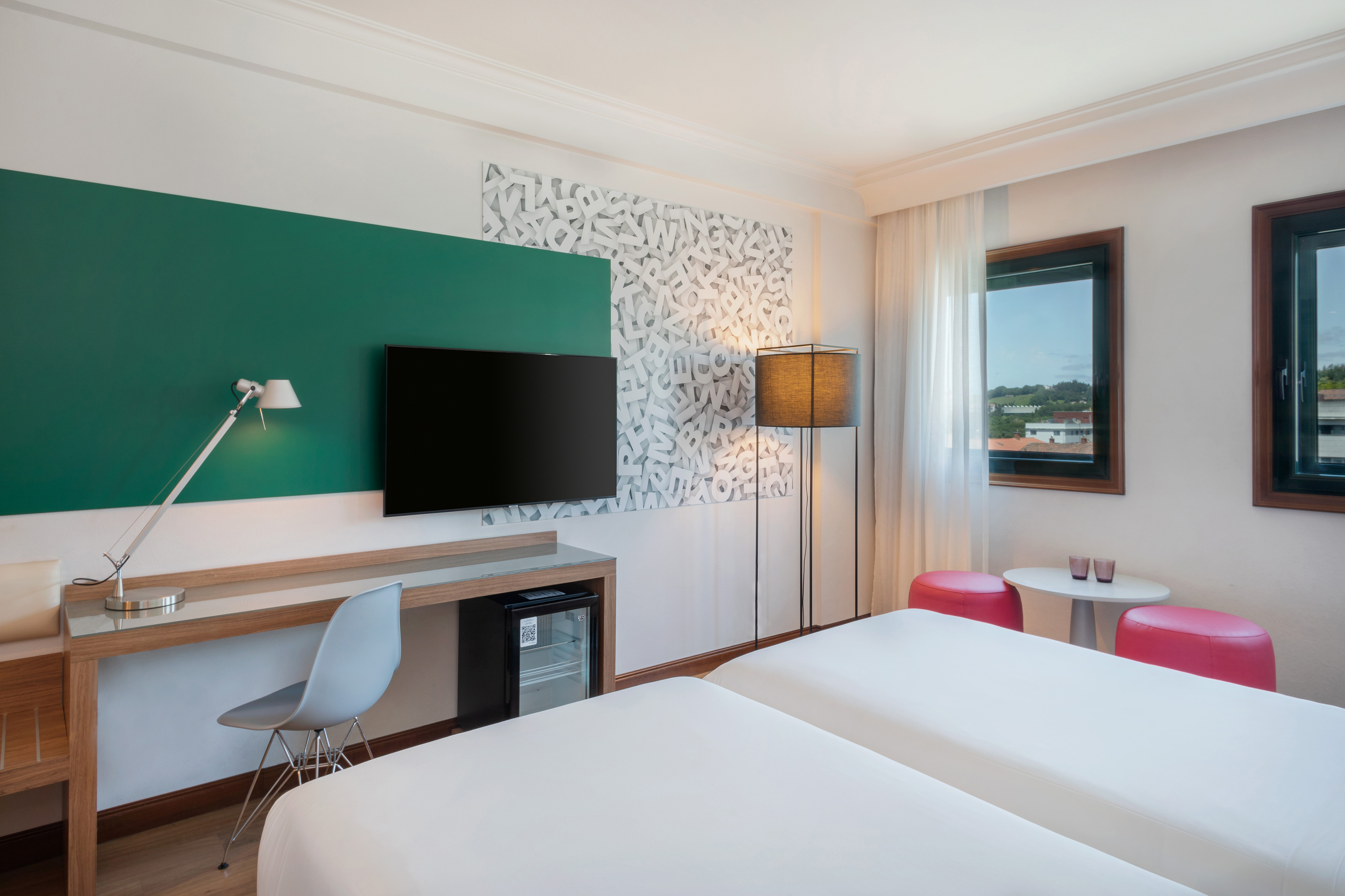Modern hotel guest room with twin beds, desk, TV, and unique wall art.