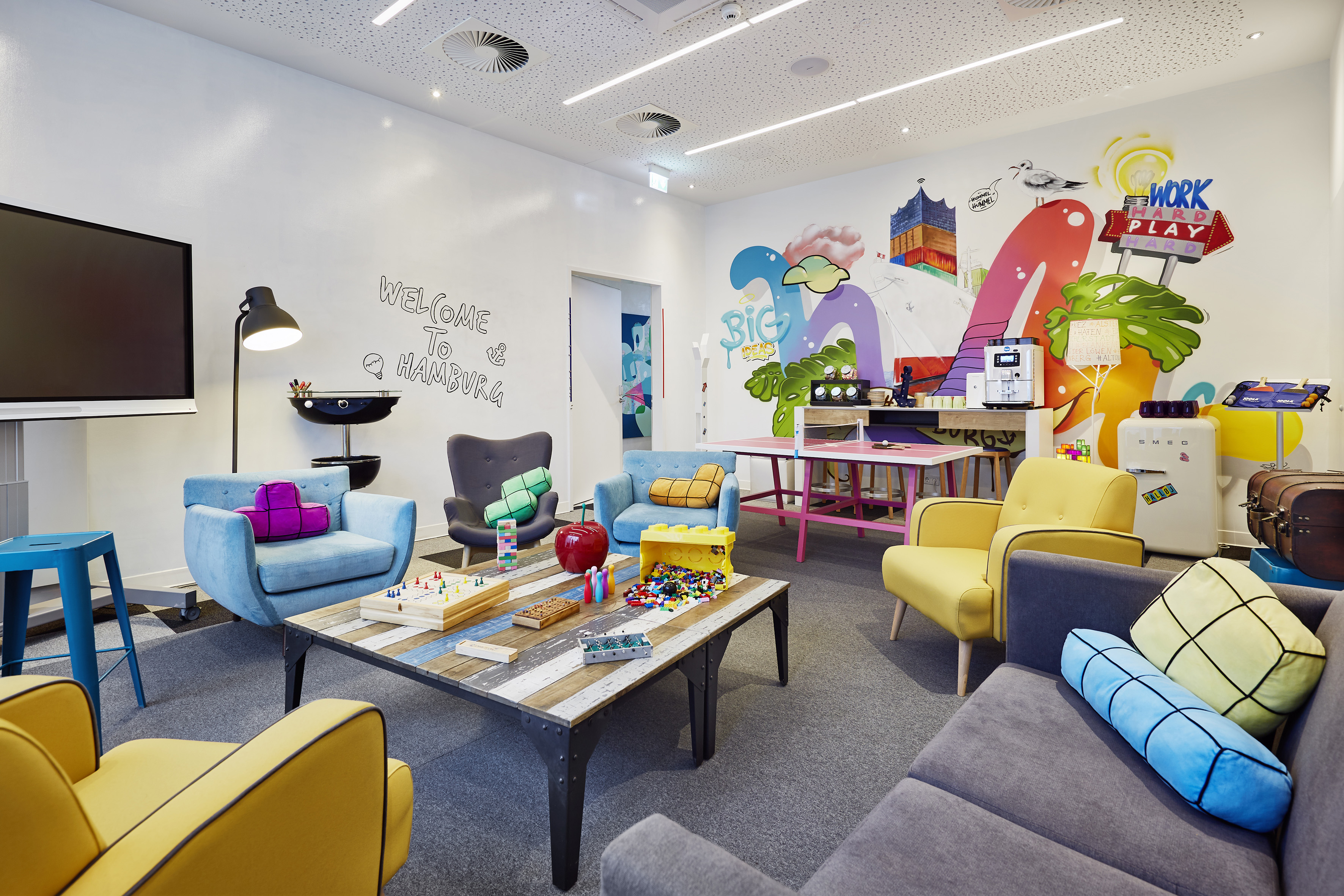 Colorful office lounge with games, diverse seating, and a vibrant Hamburg mural.
