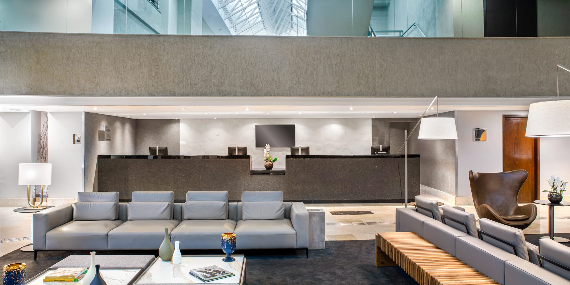 Contemporary hotel lobby with reception, grey sofas, and mezzanine level.