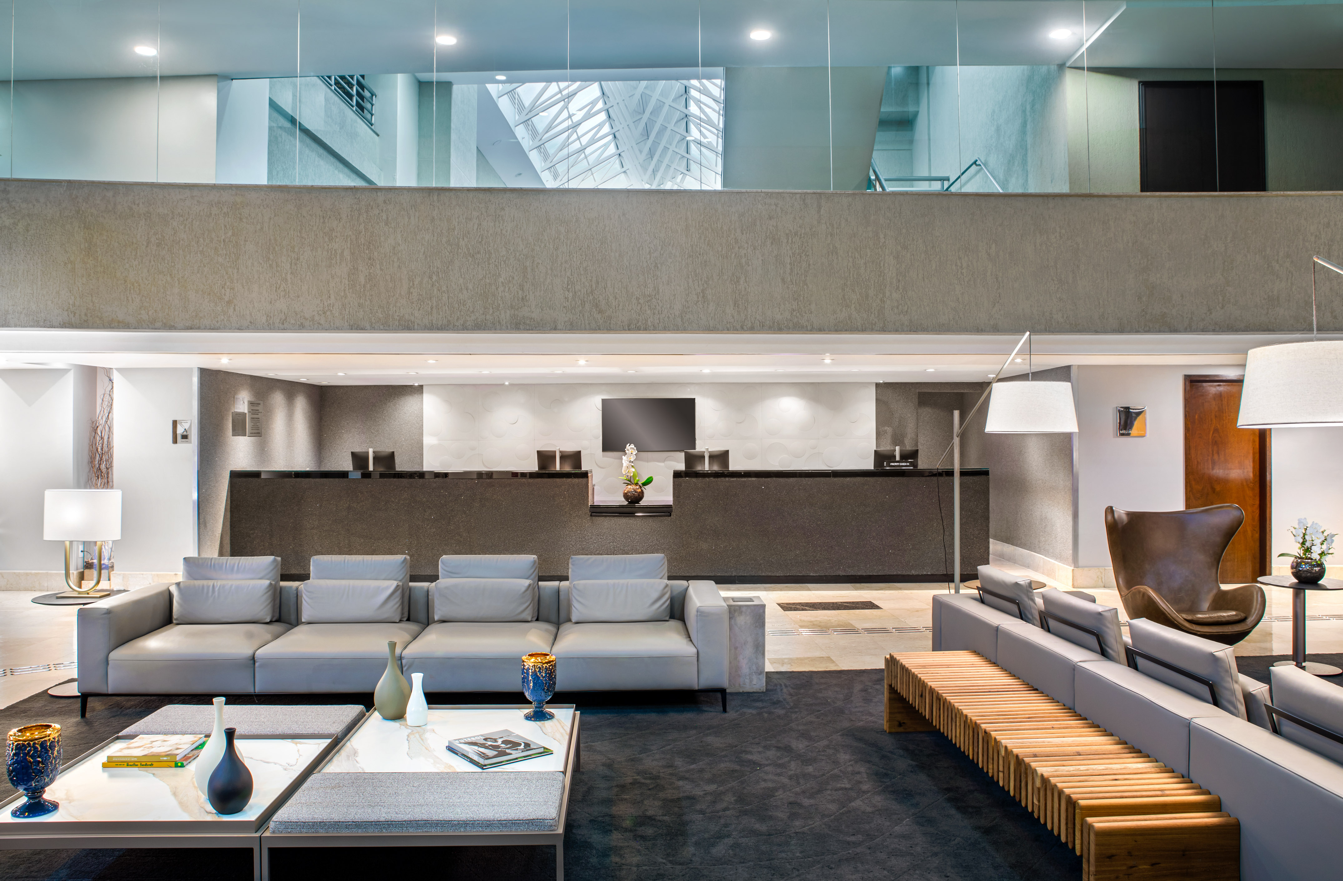 Contemporary hotel lobby with reception, grey sofas, and mezzanine level.