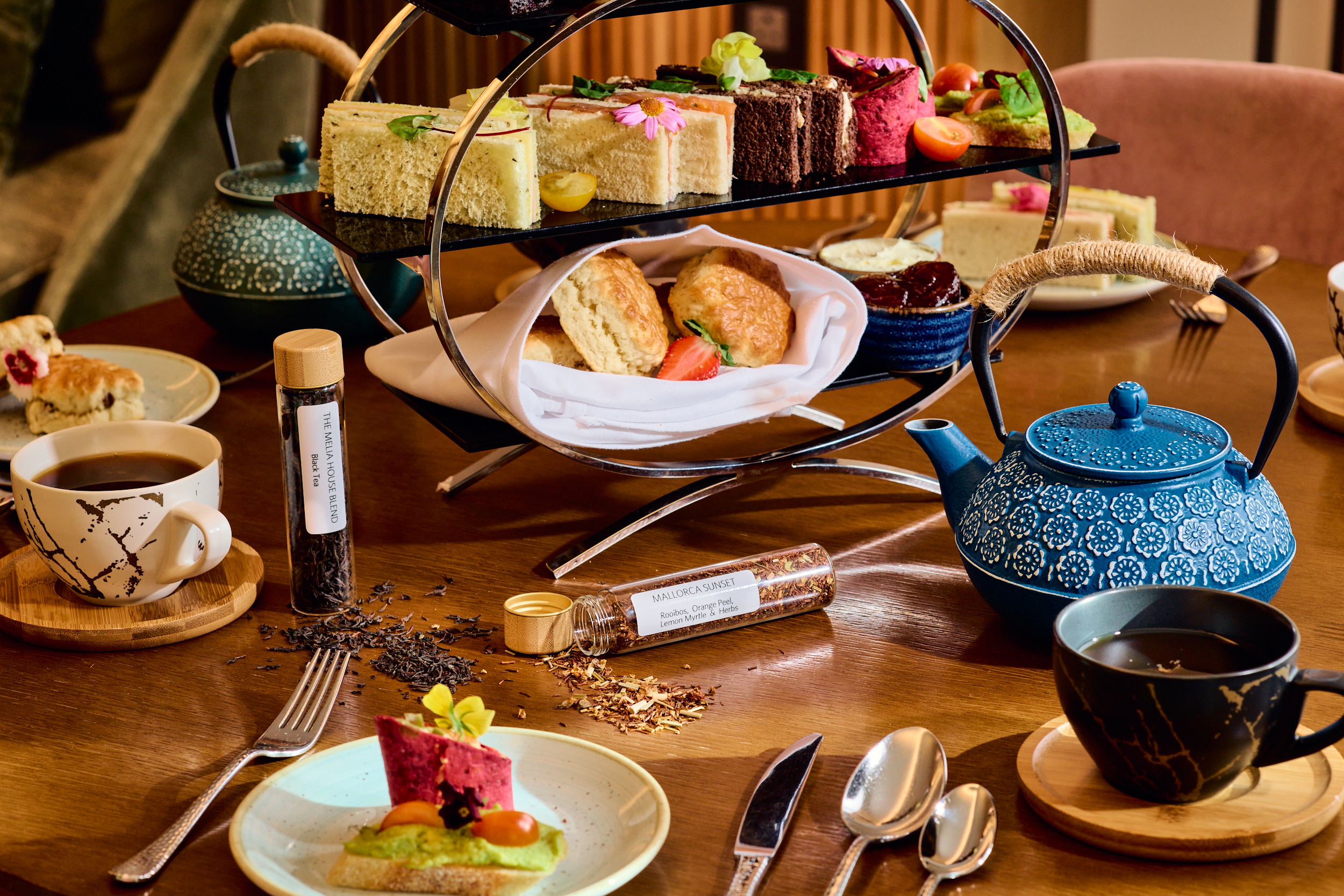 Afternoon tea with sandwiches, scones, cakes on tiered stand, and teapots.
