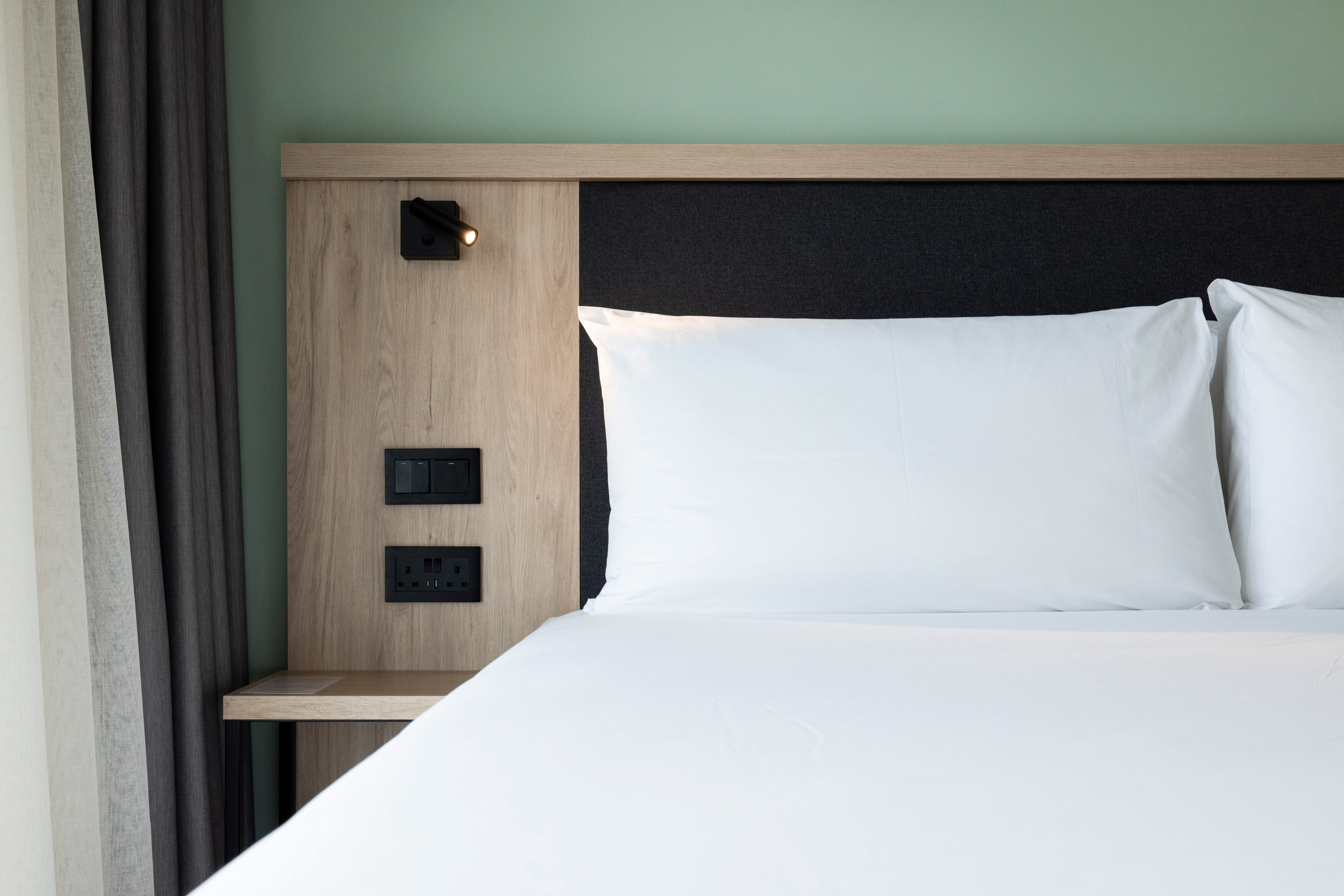 Modern hotel bed, white linens, wood headboard, integrated lamp, outlets.