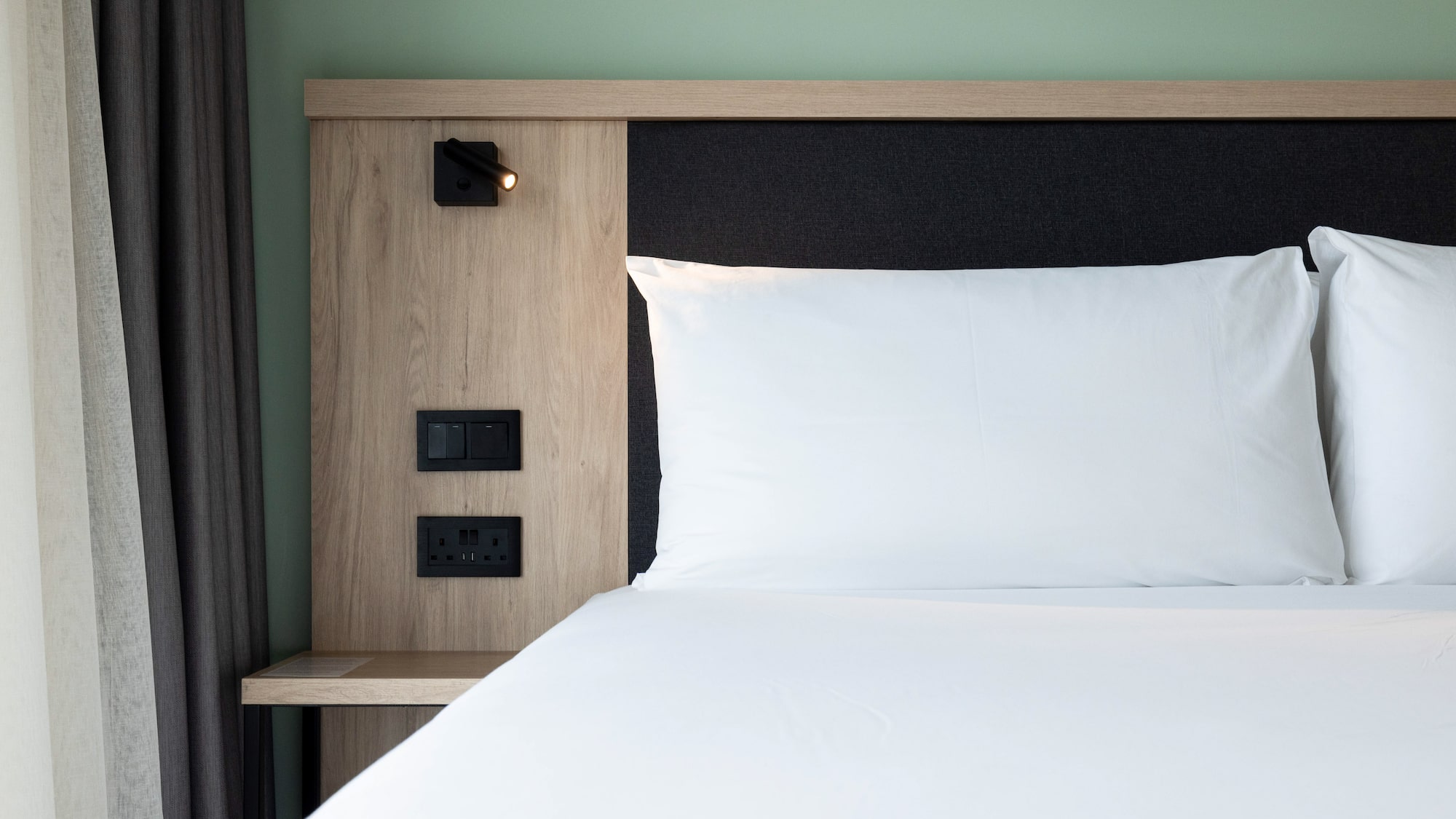 Modern hotel bed, white linens, wood headboard, integrated lamp, outlets.