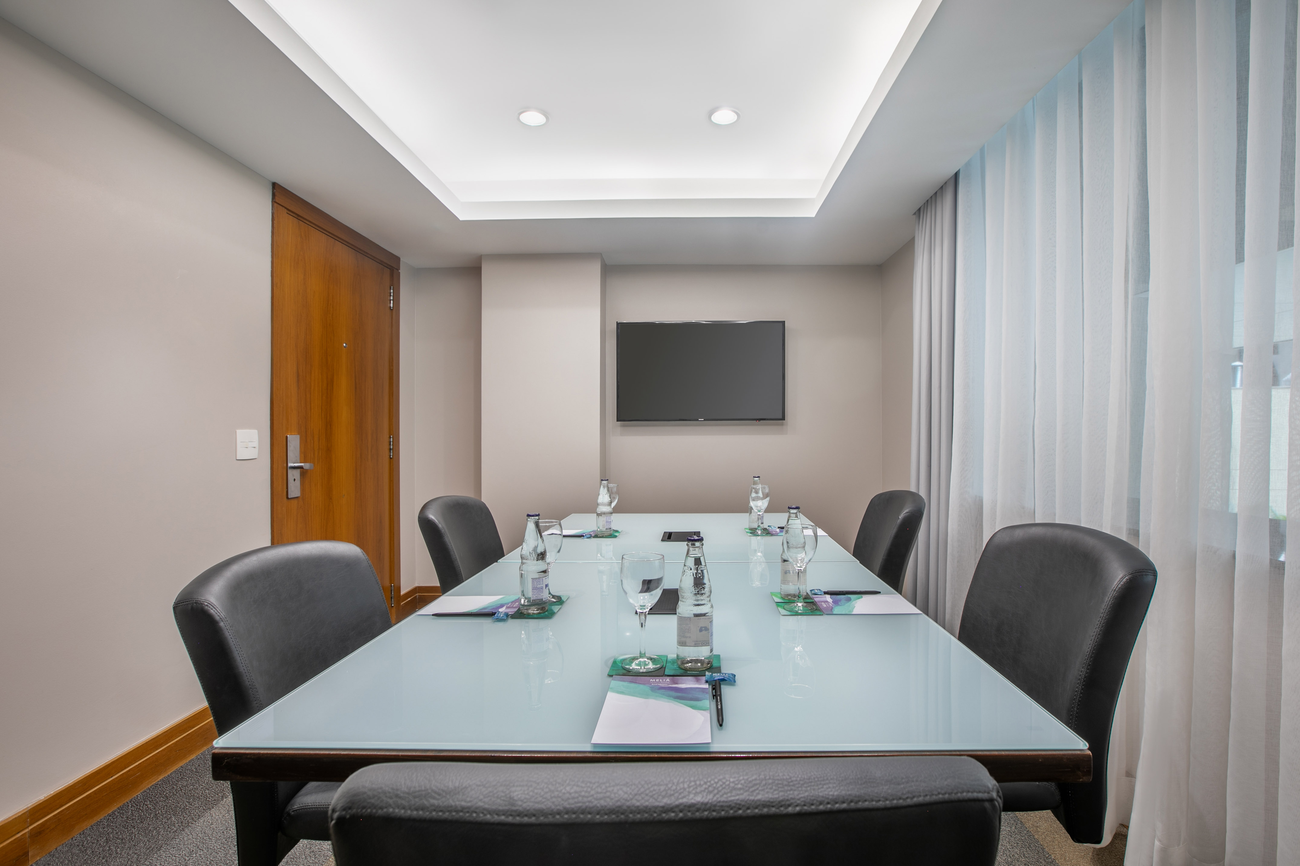 Executive conference room with modern glass table, leather chairs, and TV screen.
