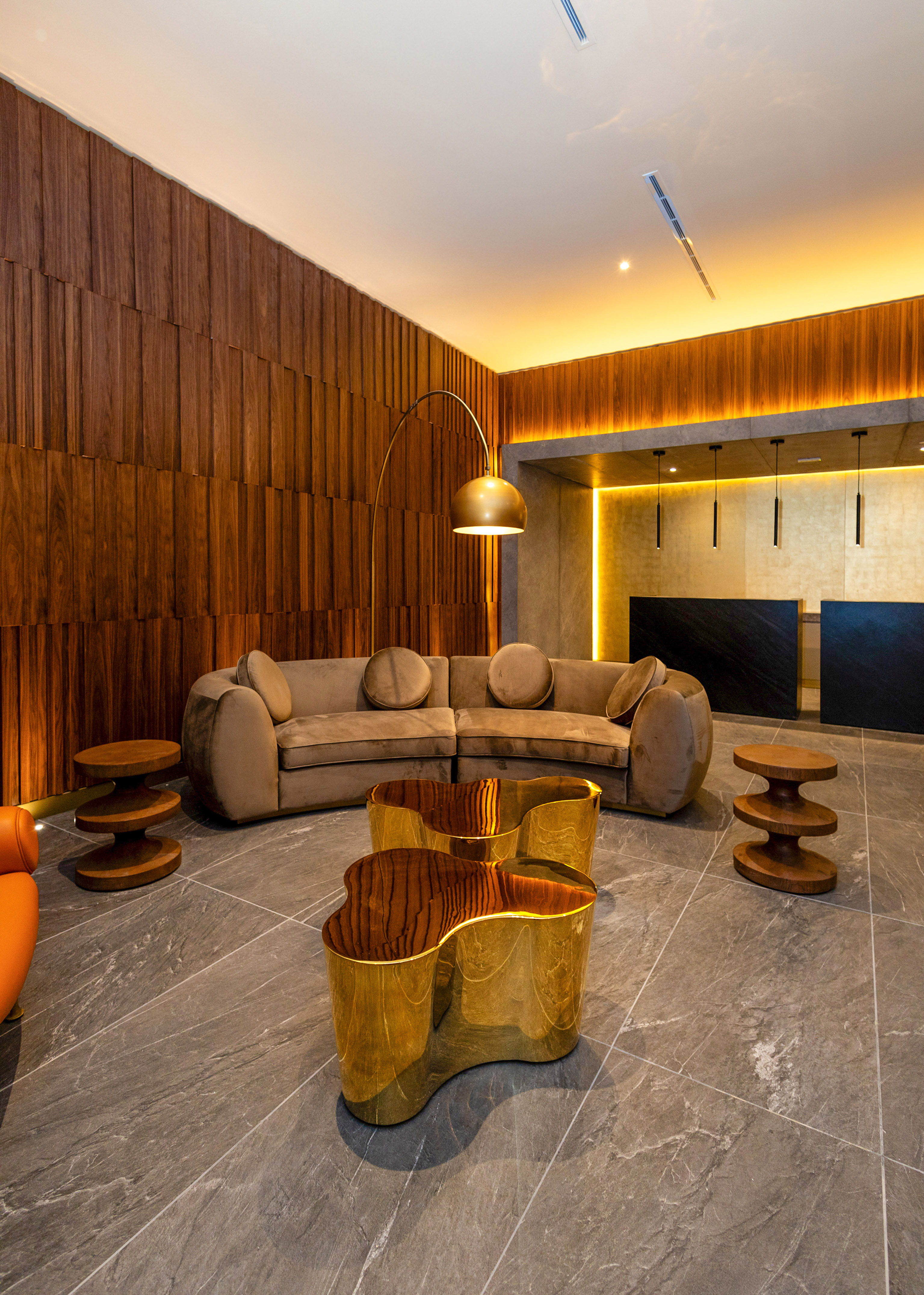 Upscale lounge with velvet sofa, wavy gold tables, and warm wood paneling.