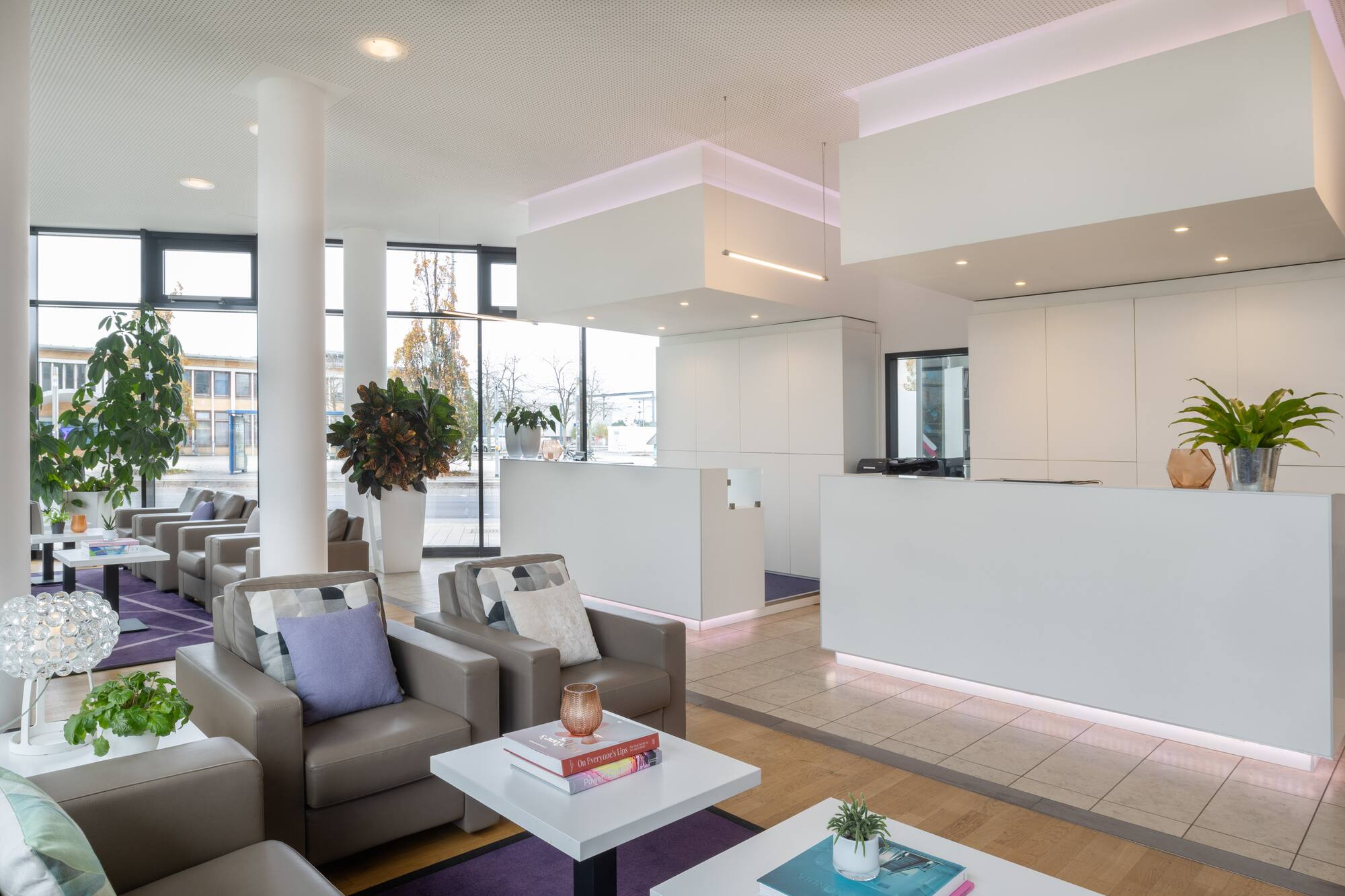 Modern office lobby with white reception desks, leather chairs, and plants.