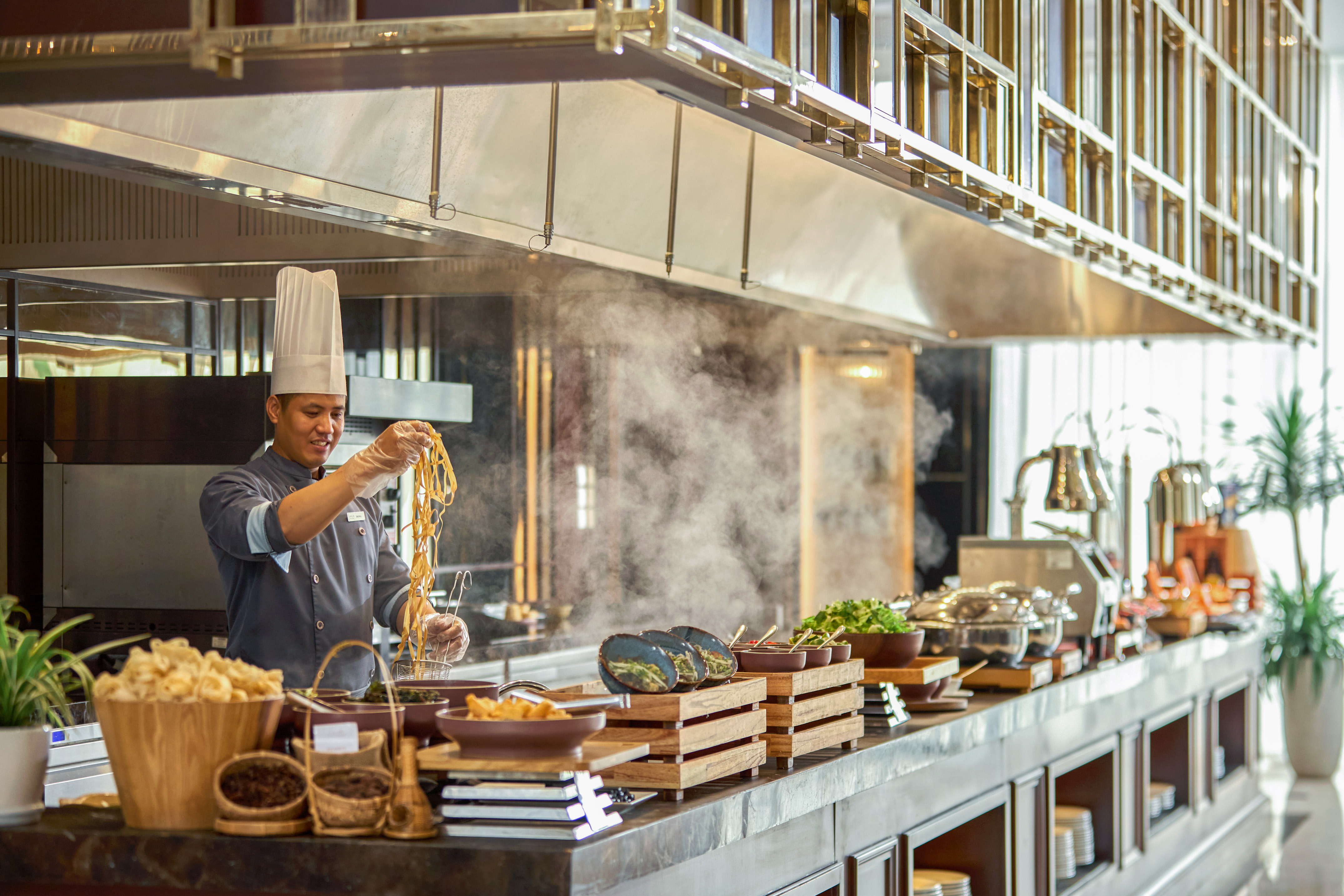 Chef preparing fresh noodles at a hotel buffet live cooking station.