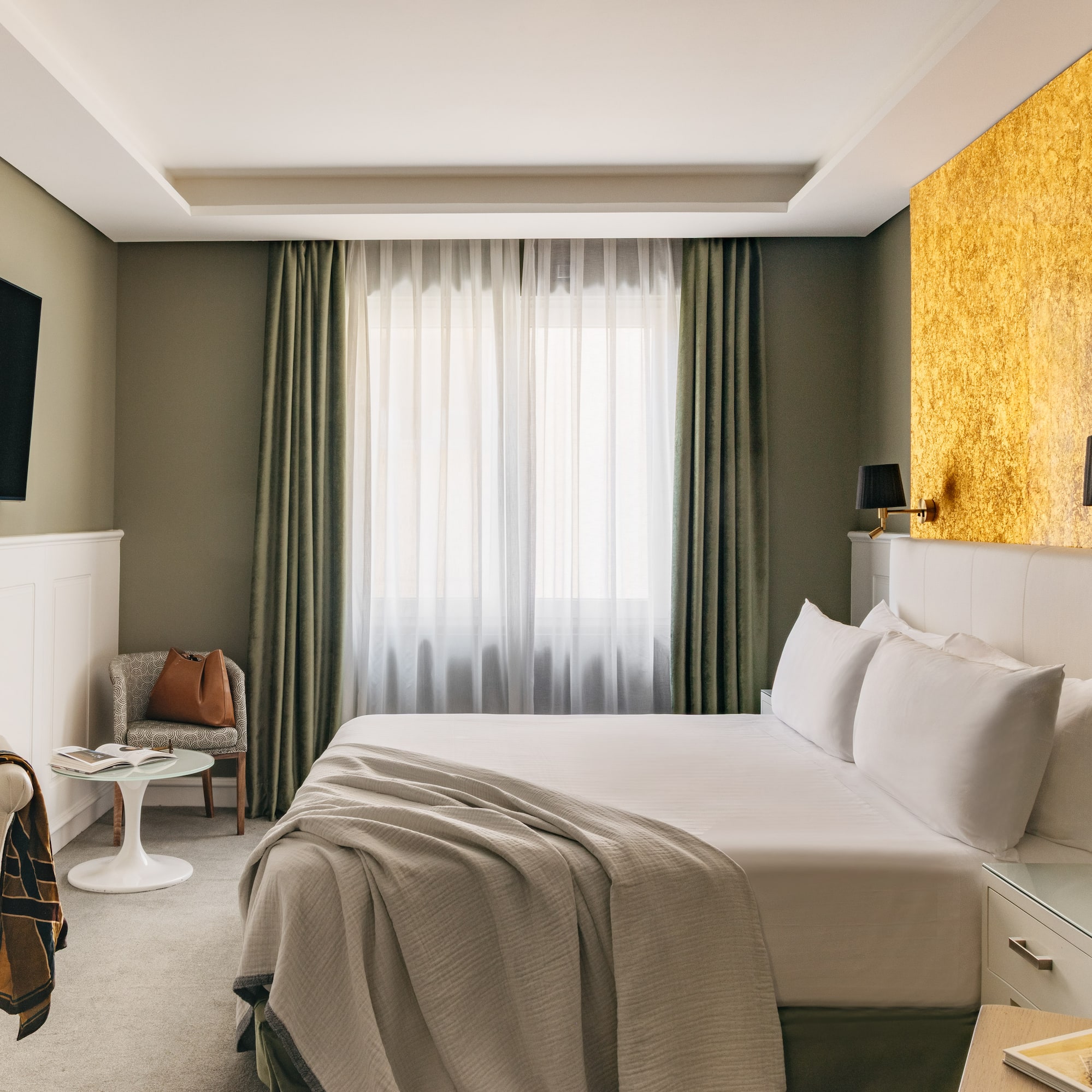 Habitación de hotel moderna con cama king-size, pared dorada y TV.