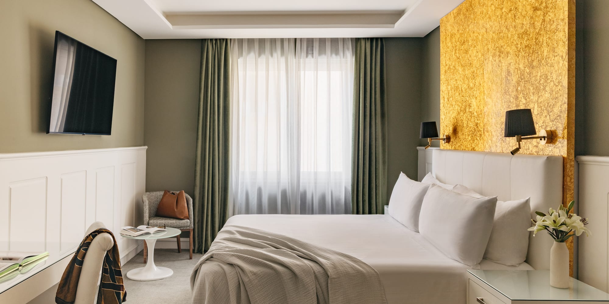 Habitación de hotel moderna con cama king-size, pared dorada y TV.
