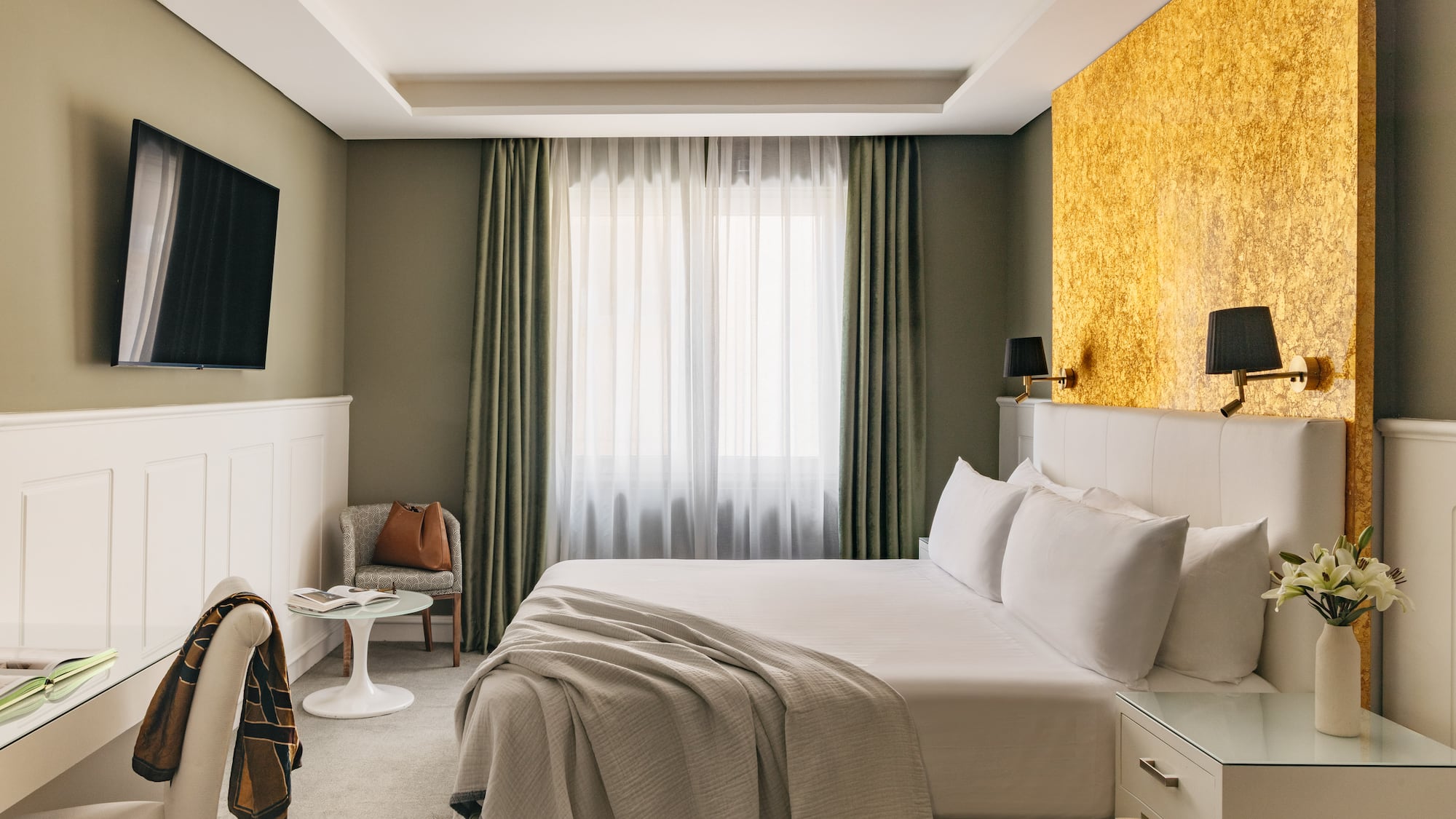 Habitación de hotel moderna con cama king-size, pared dorada y TV.