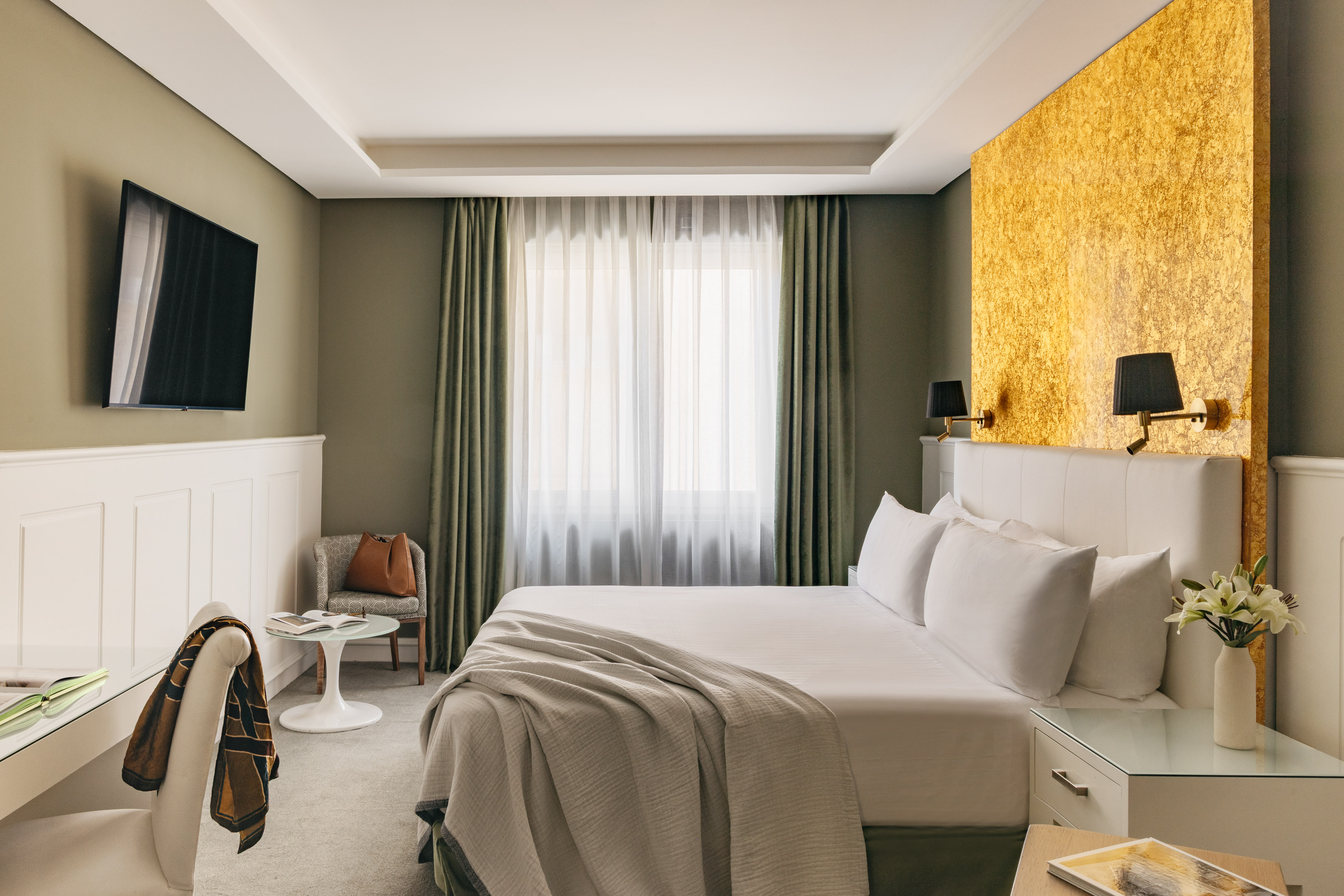 Habitación de hotel moderna con cama king-size, pared dorada y TV.
