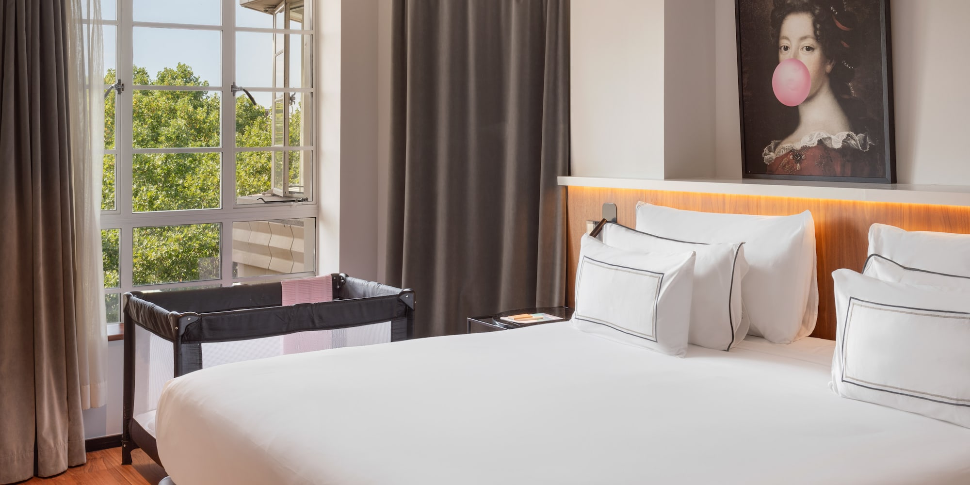Hotel room with large bed, baby travel crib, and window overlooking trees.