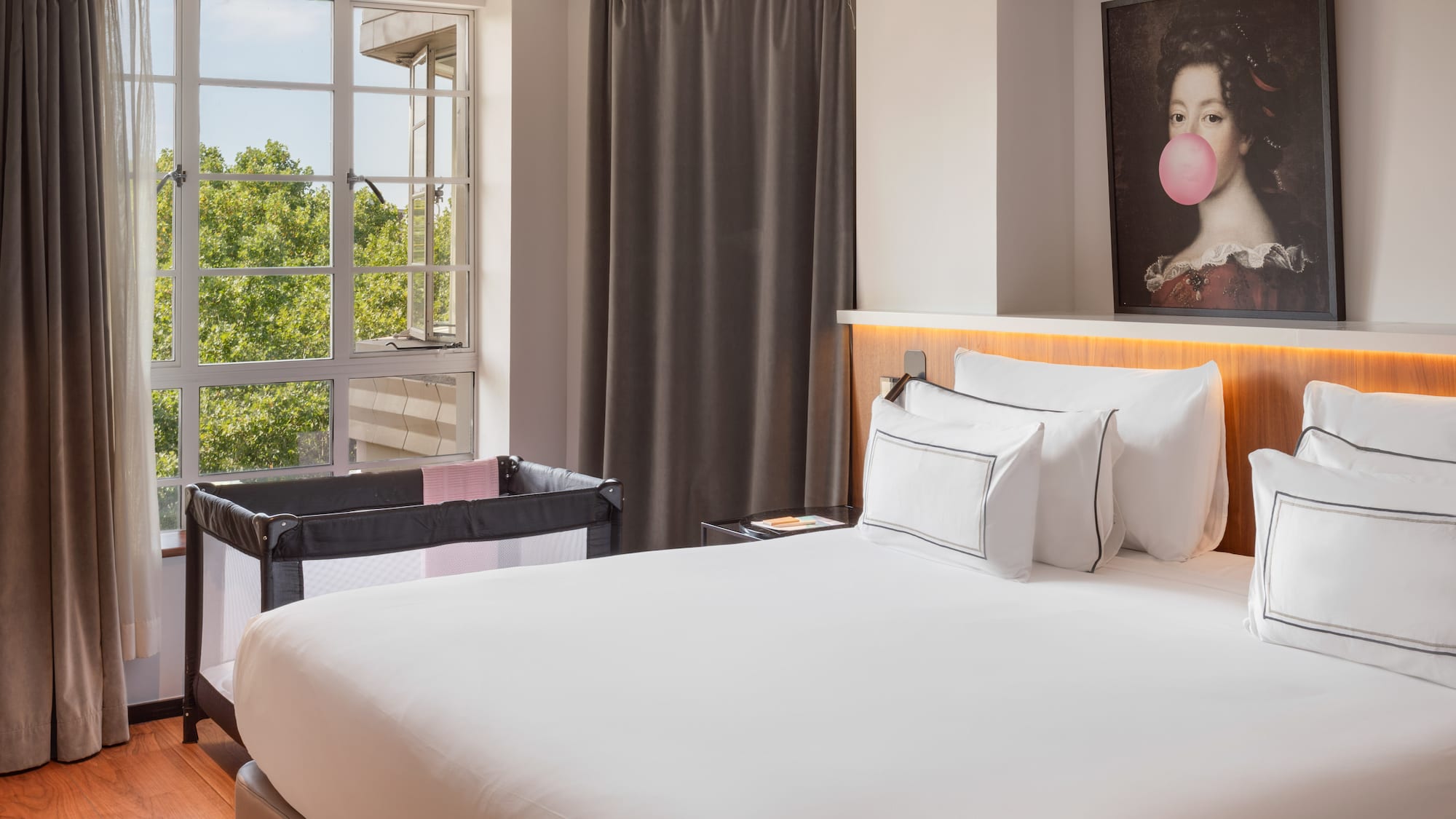 Hotel room with large bed, baby travel crib, and window overlooking trees.