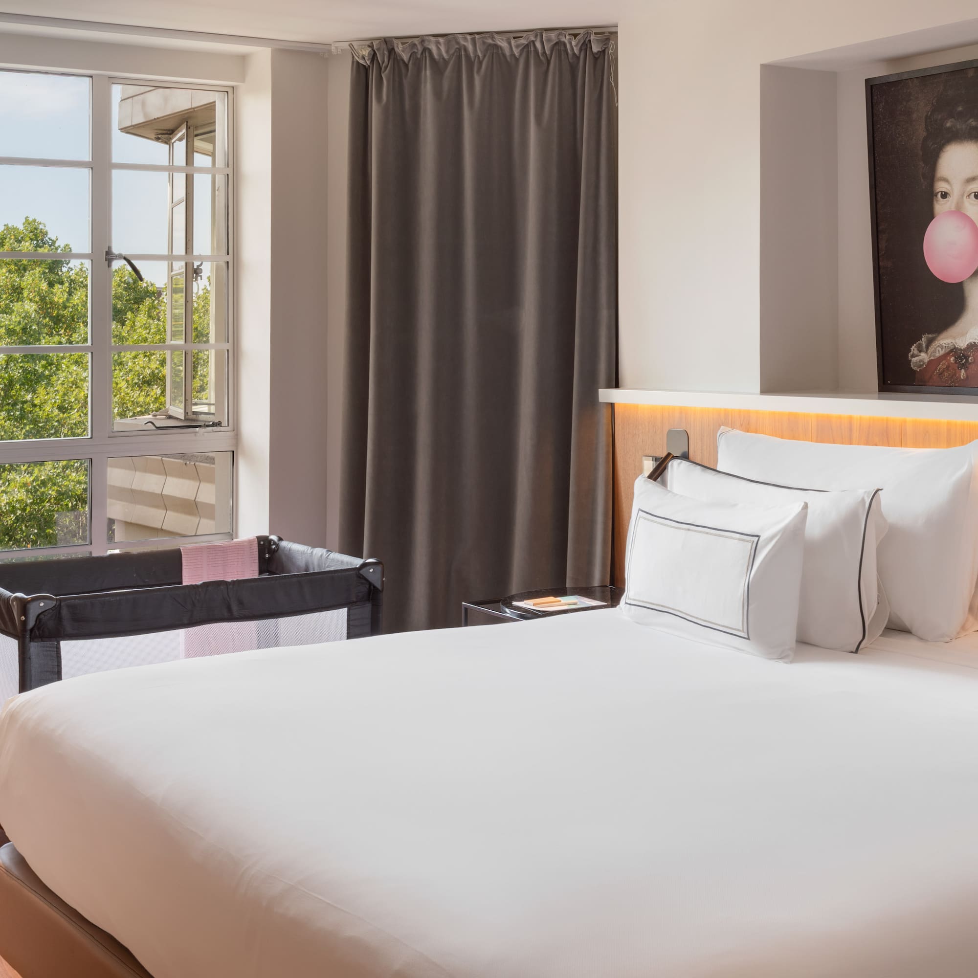 Hotel room with large bed, baby travel crib, and window overlooking trees.
