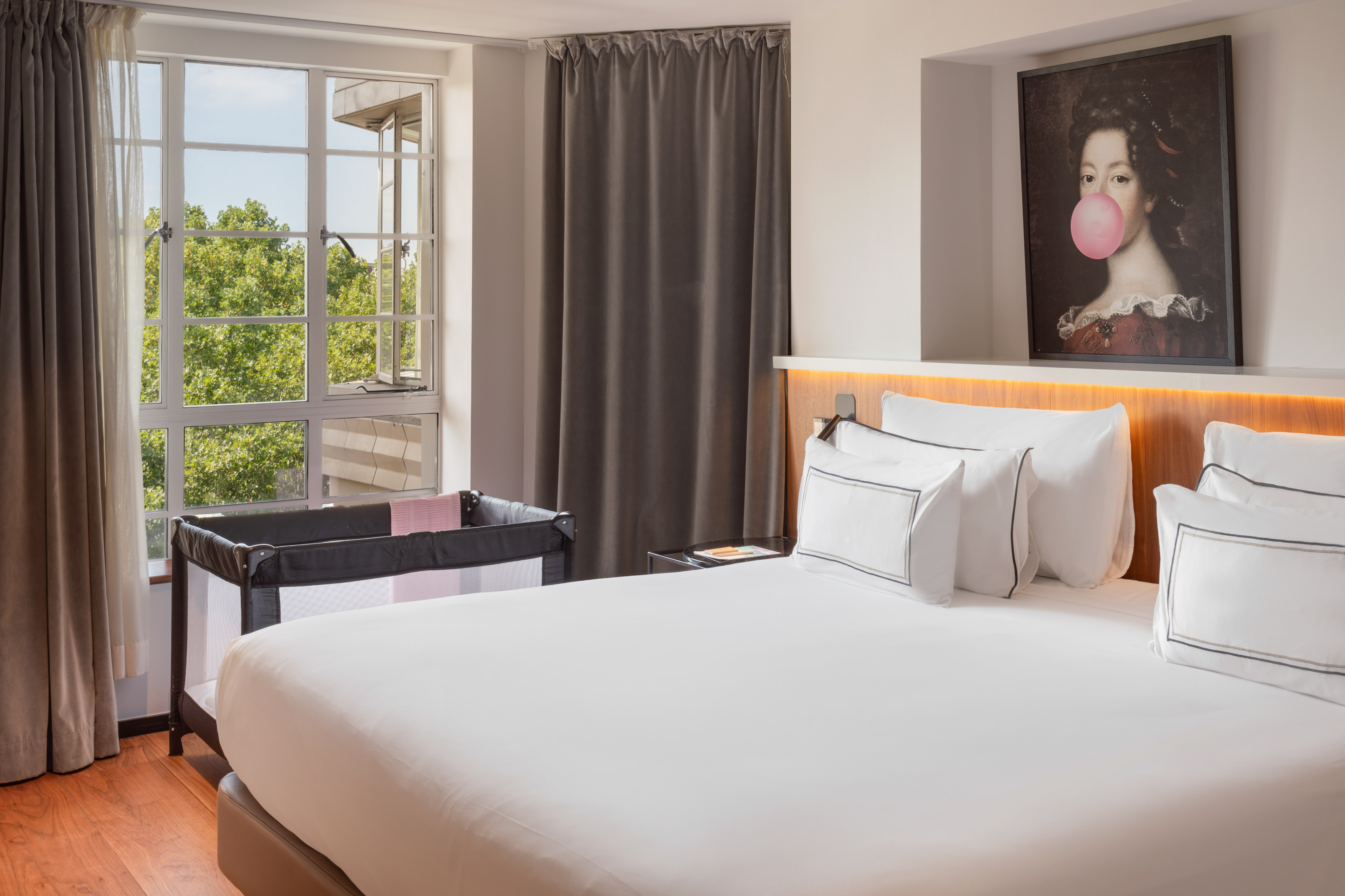 Hotel room with large bed, baby travel crib, and window overlooking trees.