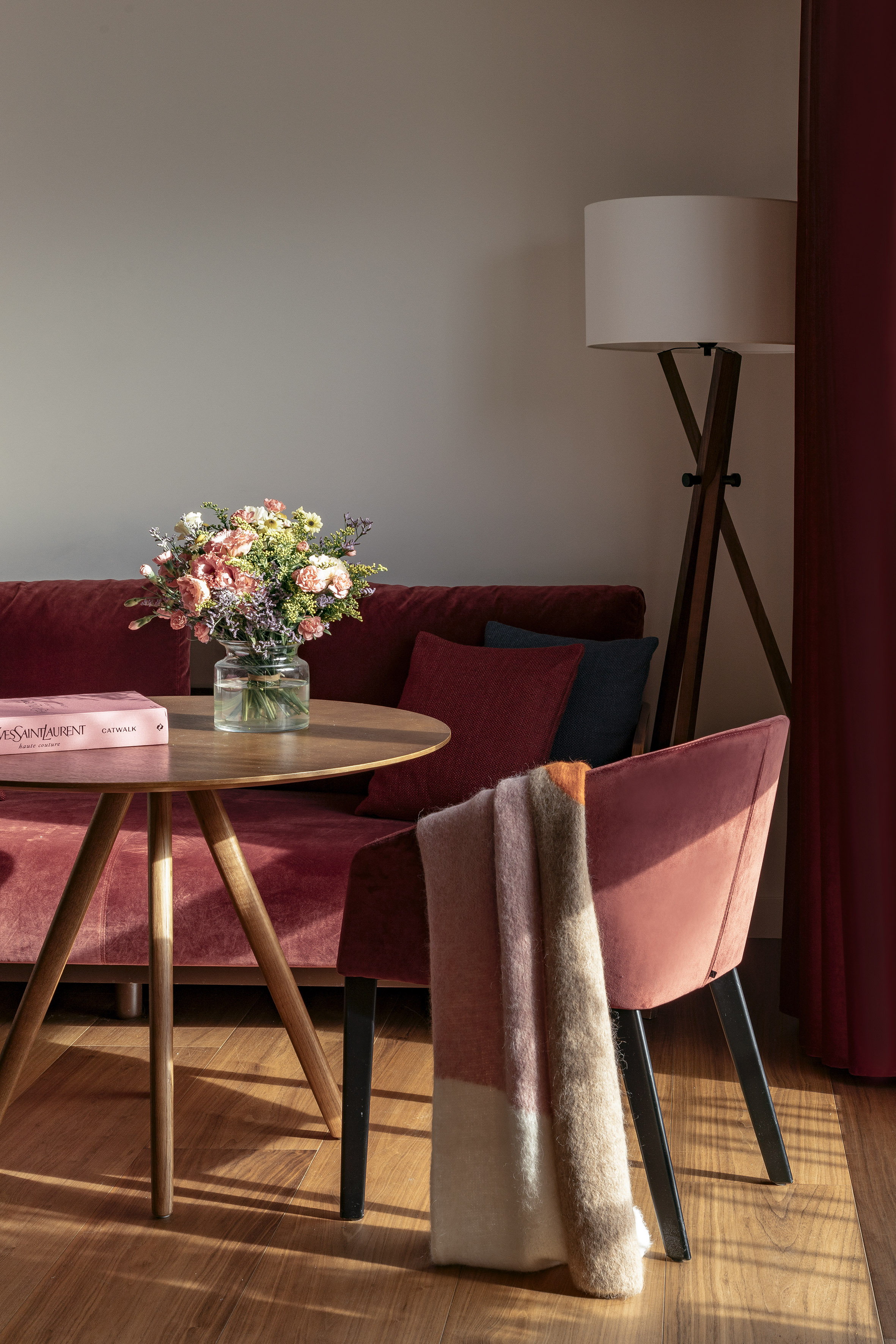 Cozy living room with red velvet sofa, coffee table, flowers, and warm decor.