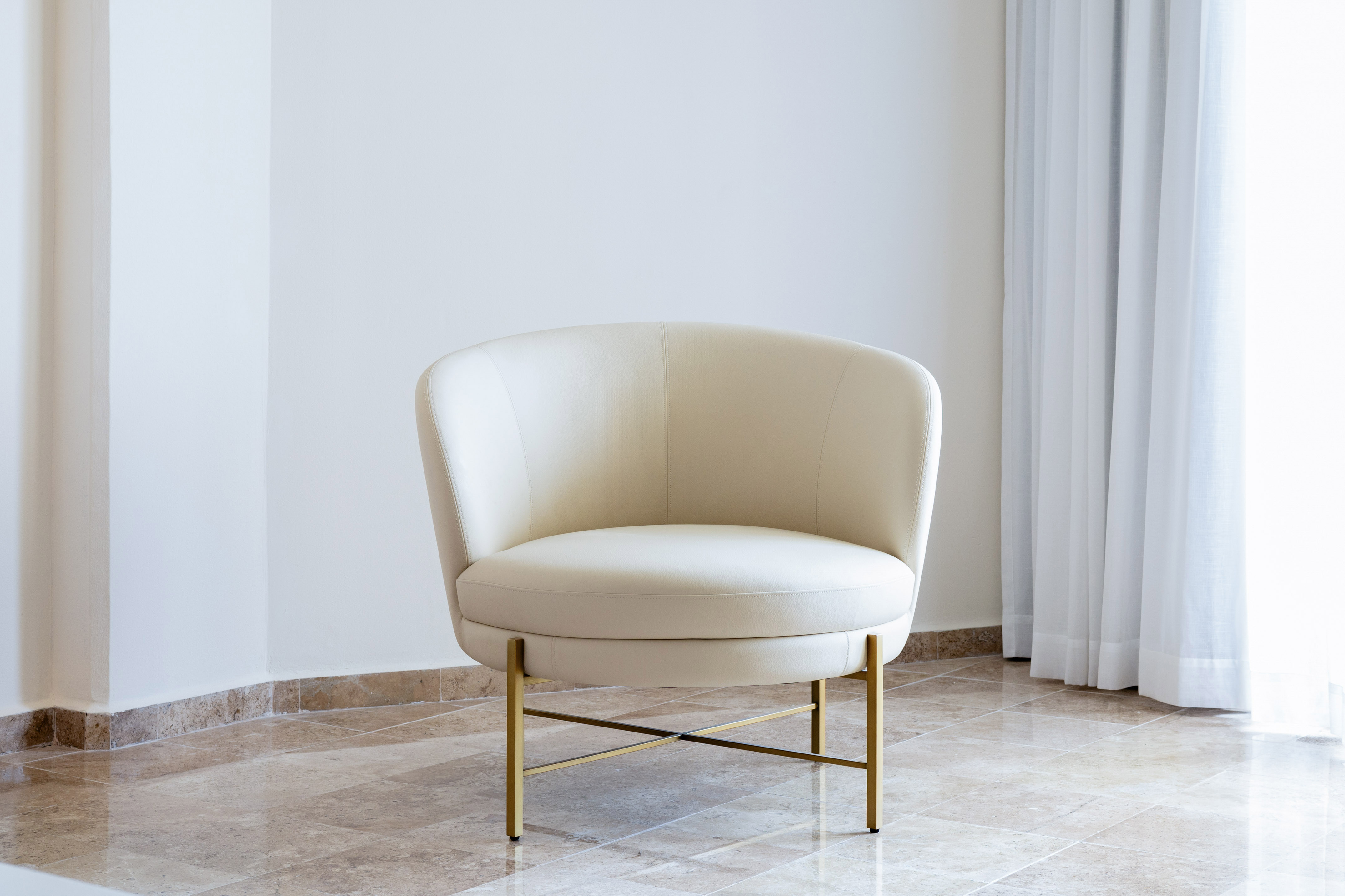 Elegant cream barrel armchair with gold legs in a bright modern interior.