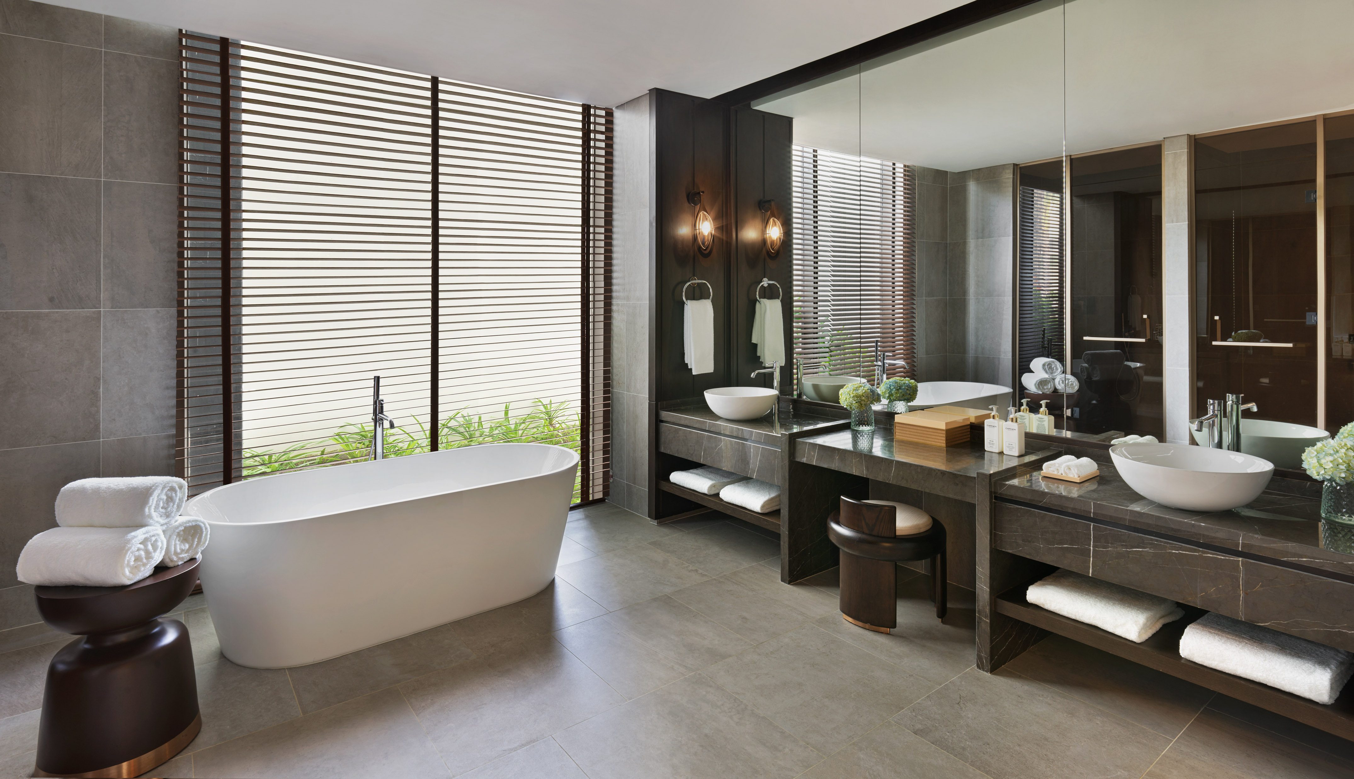 Modern luxury bathroom with freestanding tub, dual vanity, large window blinds.