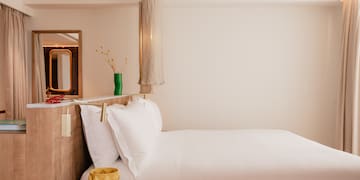 a bed with white sheets and a yellow vase on a table