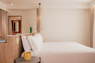 a bed with white sheets and a yellow vase on a table