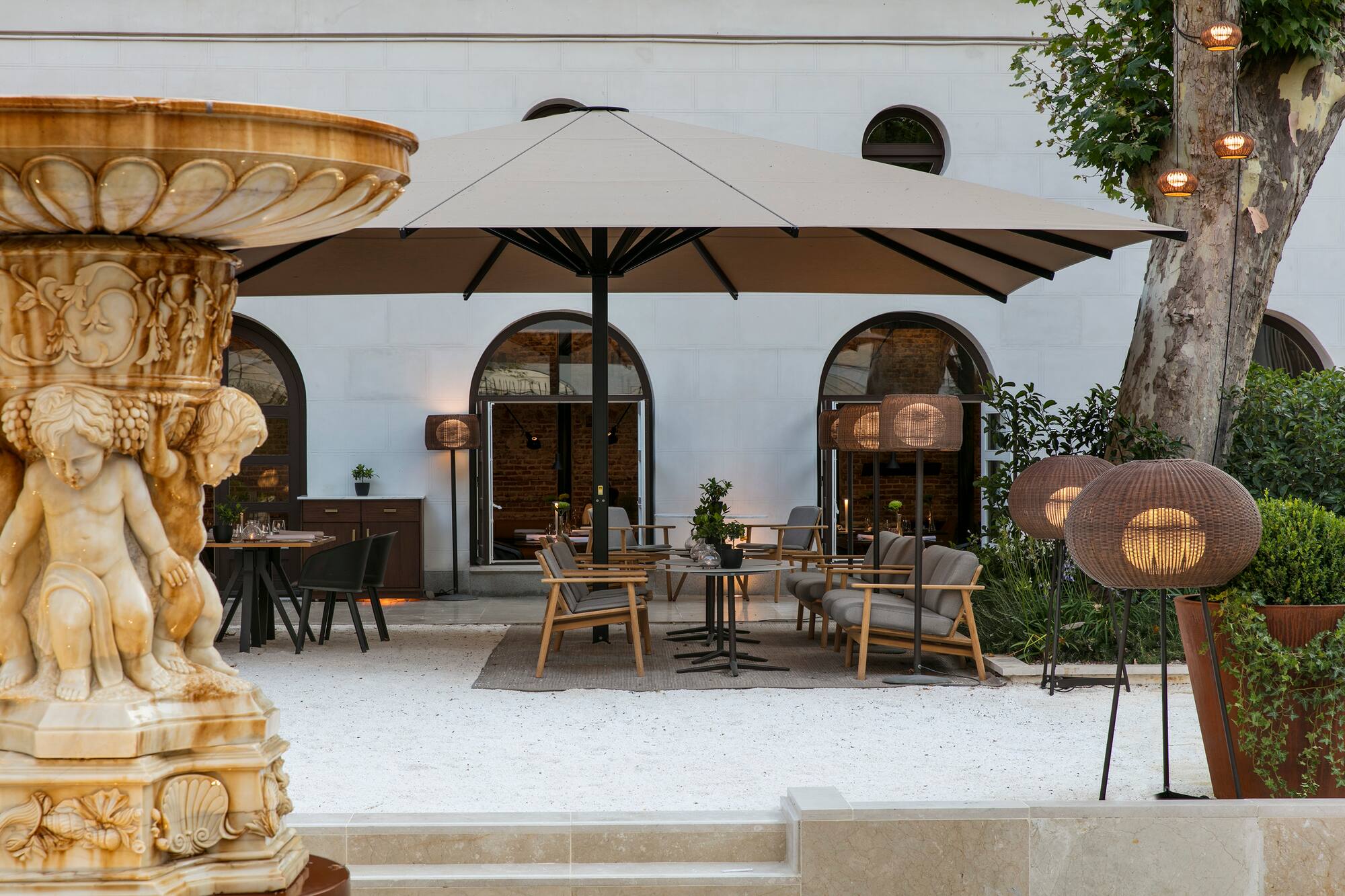 Outdoor restaurant patio, stone fountain, large umbrella, lounge seating.