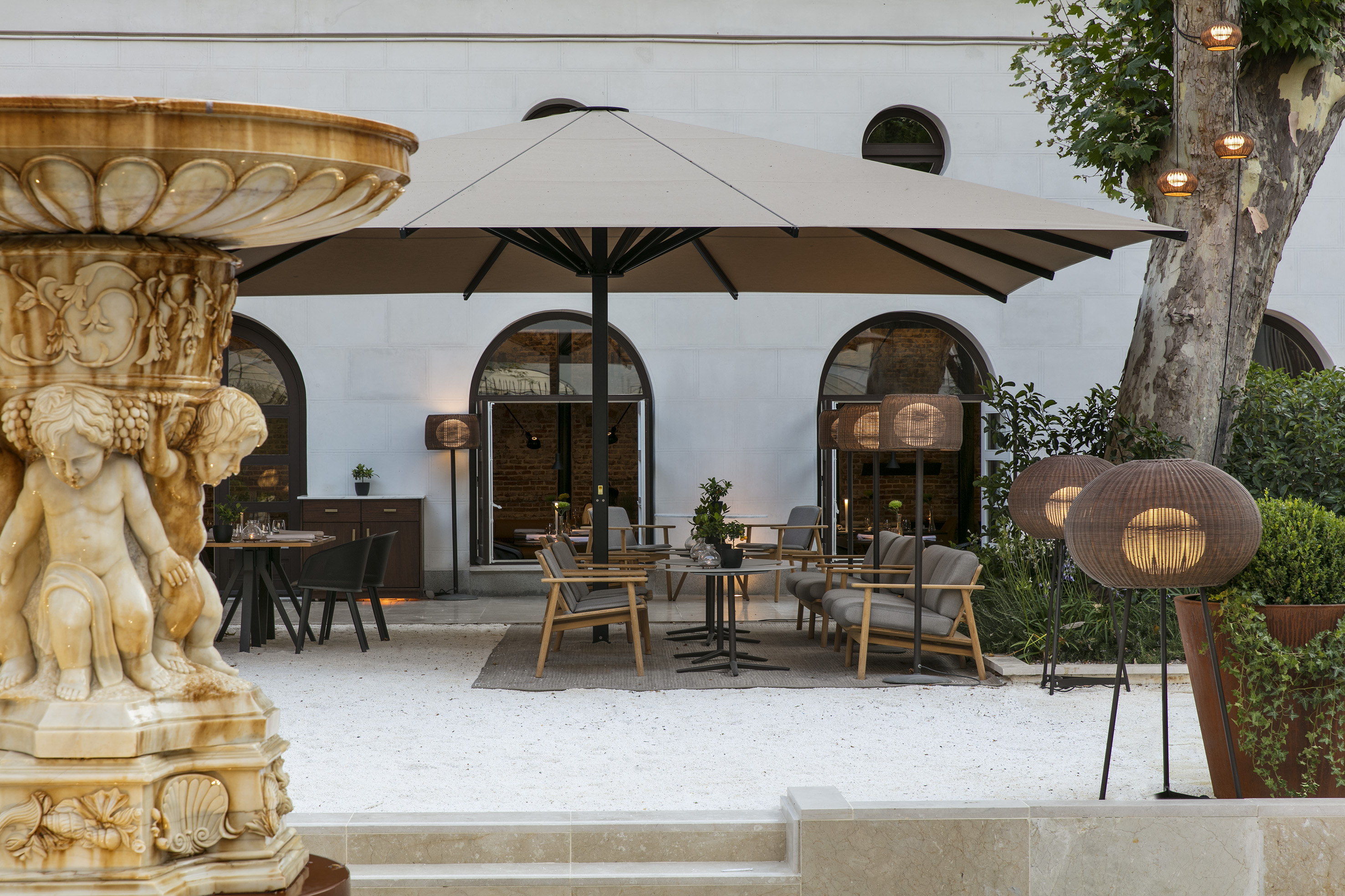 Outdoor restaurant patio, stone fountain, large umbrella, lounge seating.