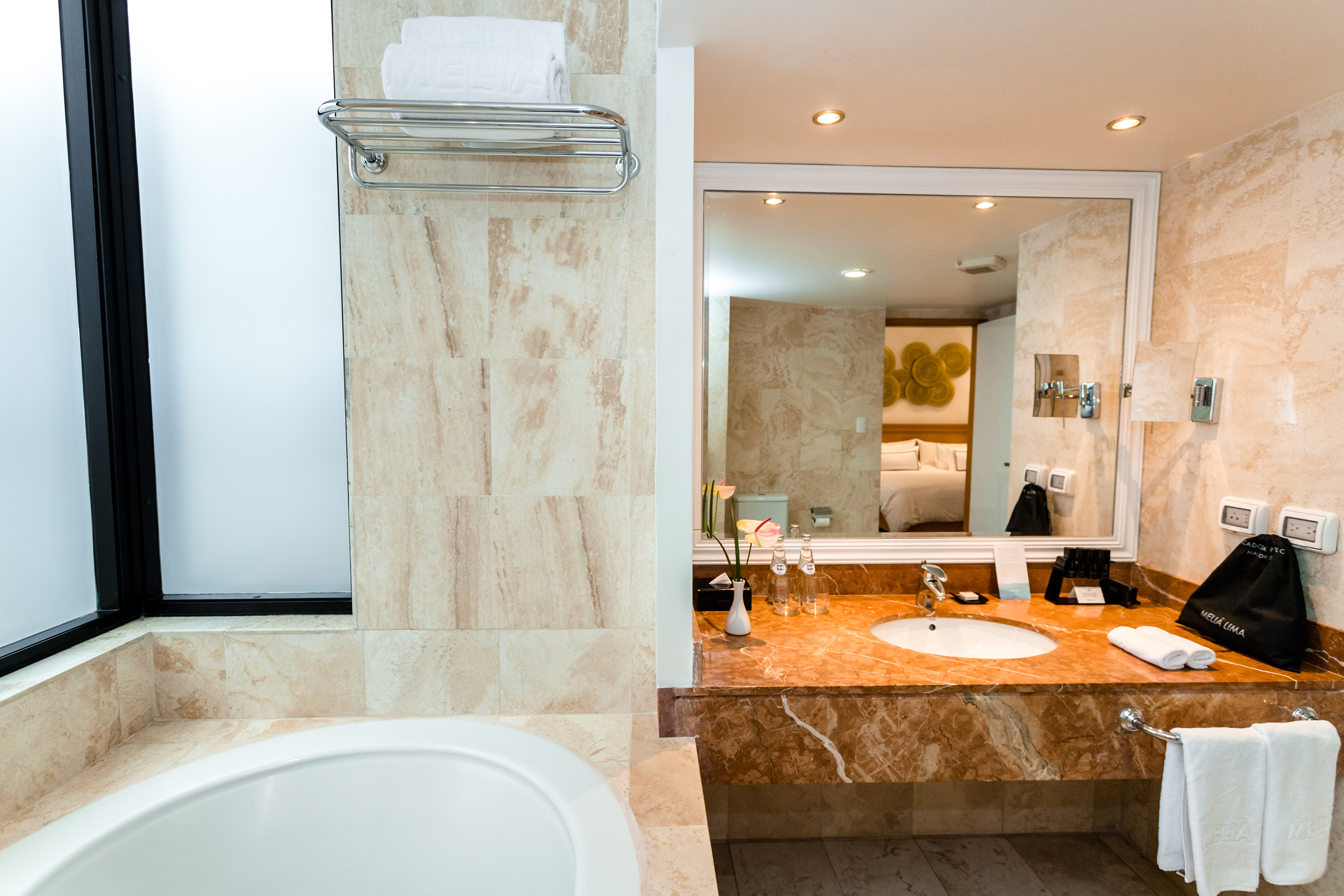 Luxury hotel bathroom with marble vanity, bathtub, and reflected bedroom.