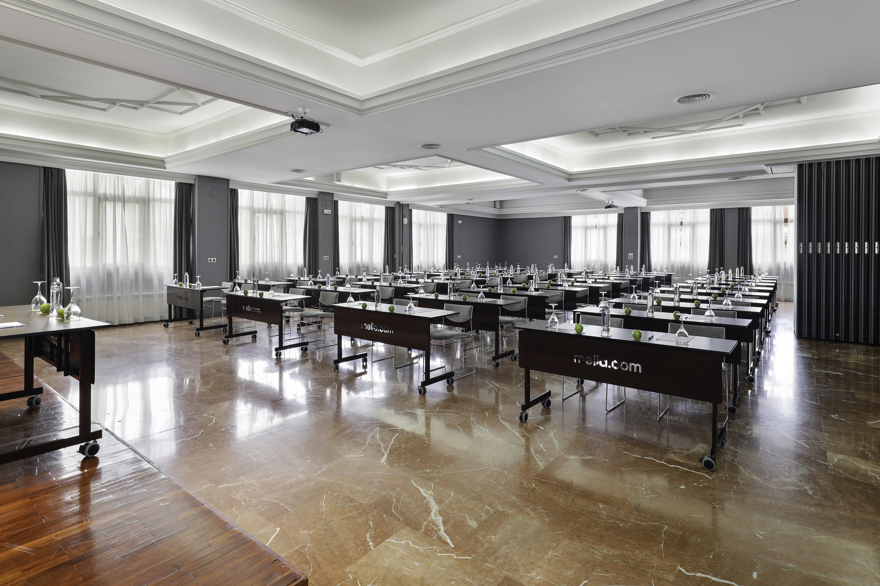 Modern hotel conference room with tables, chairs, water, and projector.