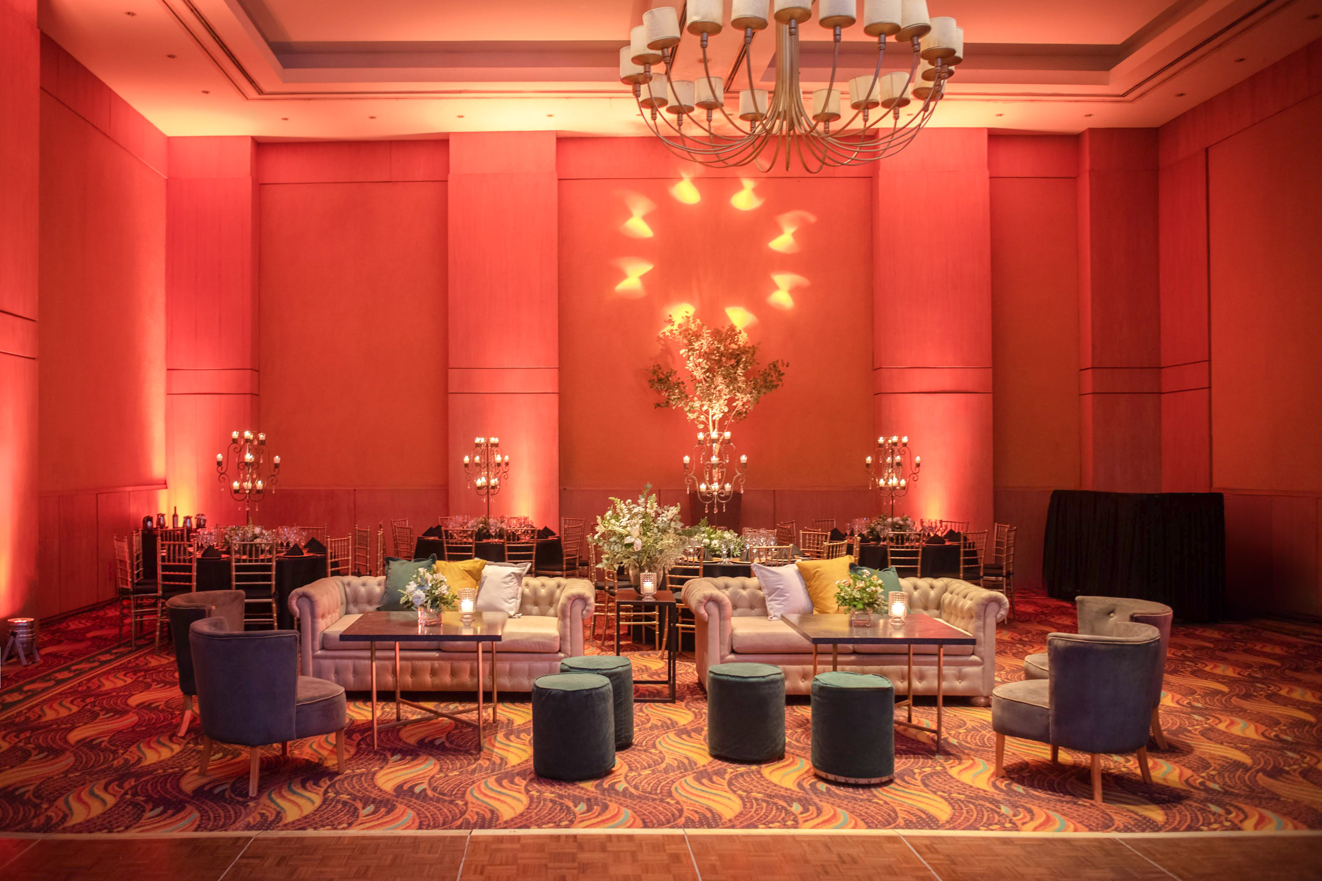 Grand ballroom set up for reception with red uplighting, lounge and dining areas.