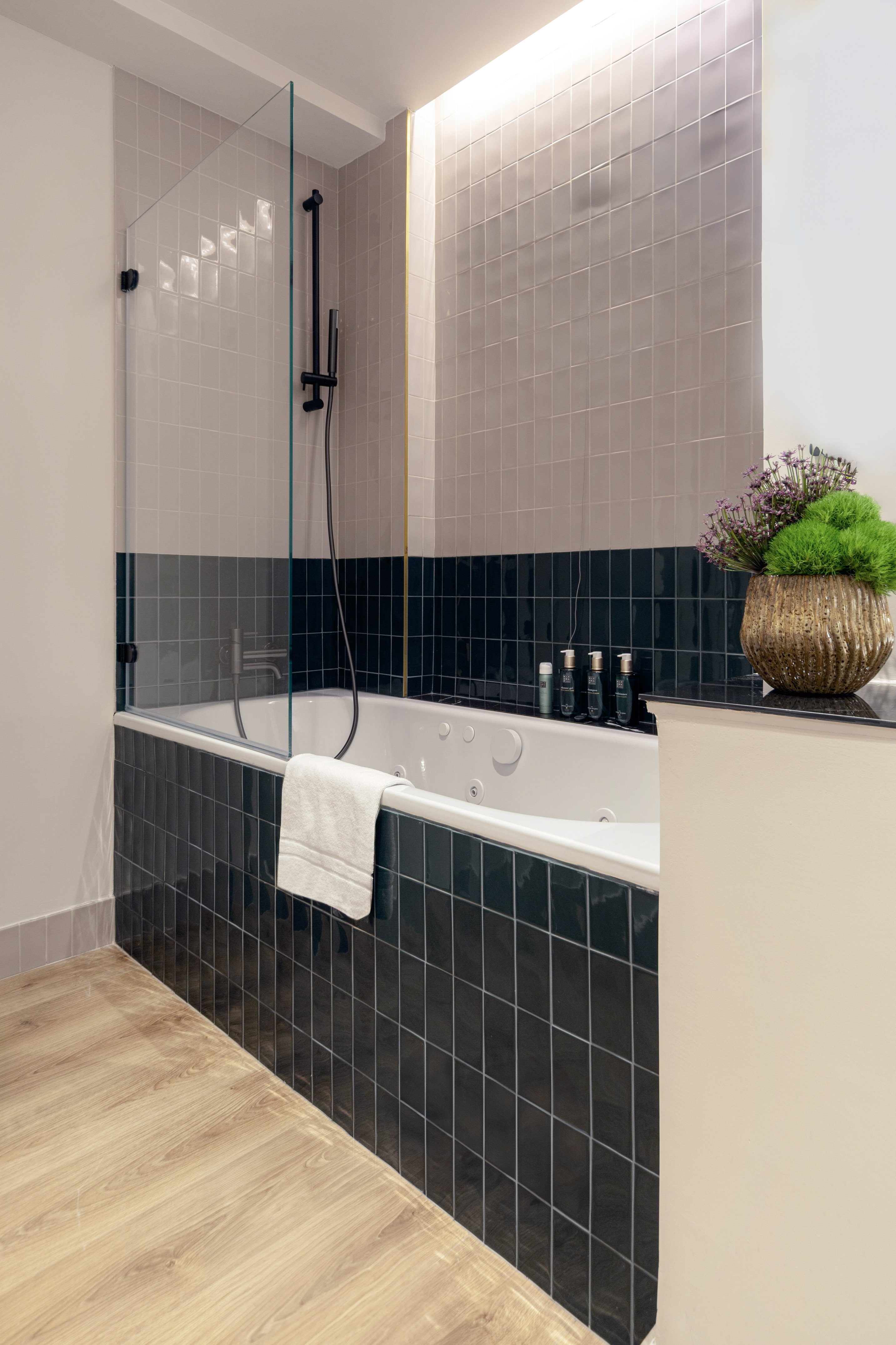 Modern bathroom with jacuzzi tub, black shower, two-tone tiles, and wood floor.
