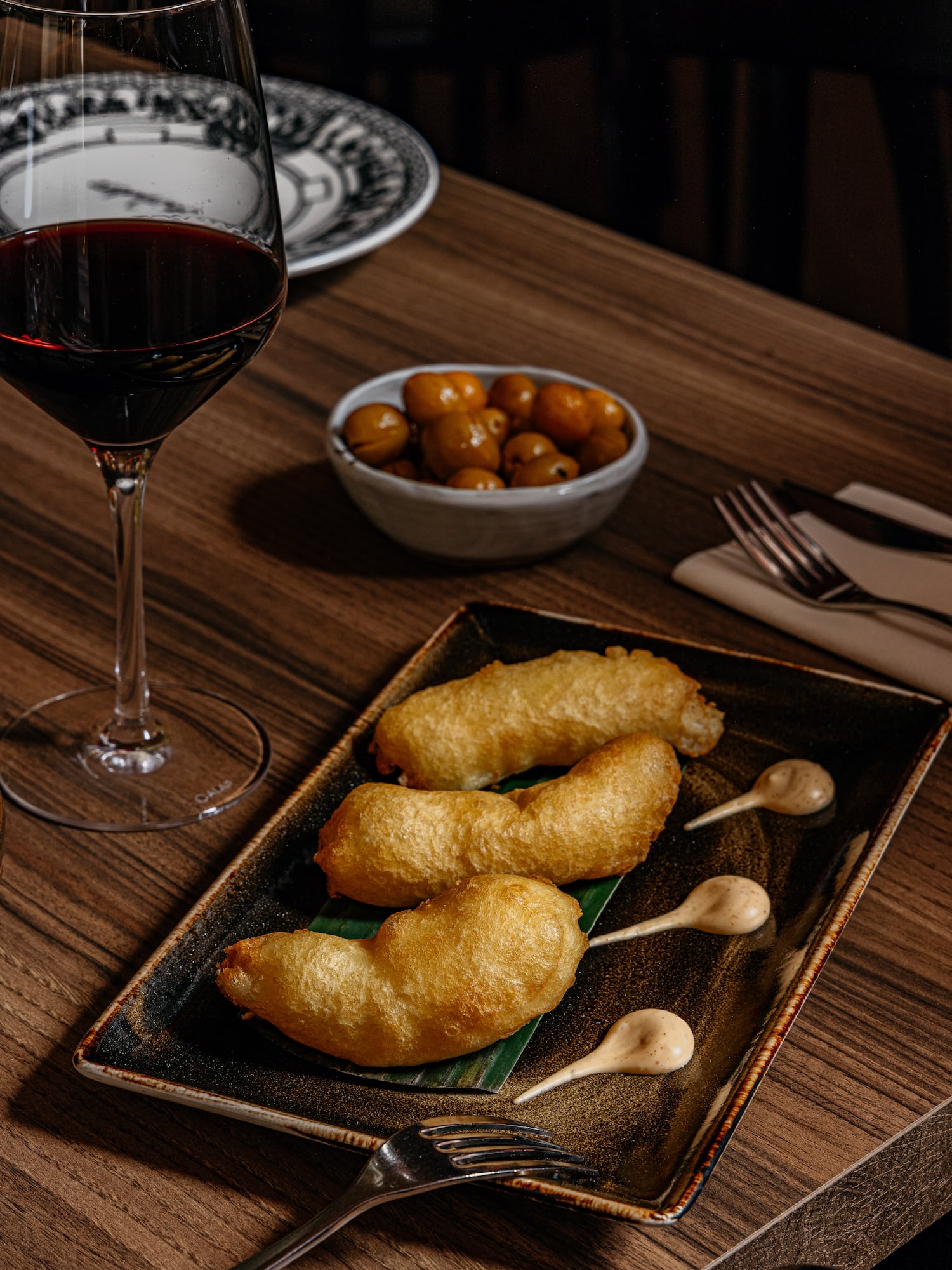 Aperitivo frito con salsa, vino tinto y aceitunas en mesa de madera.