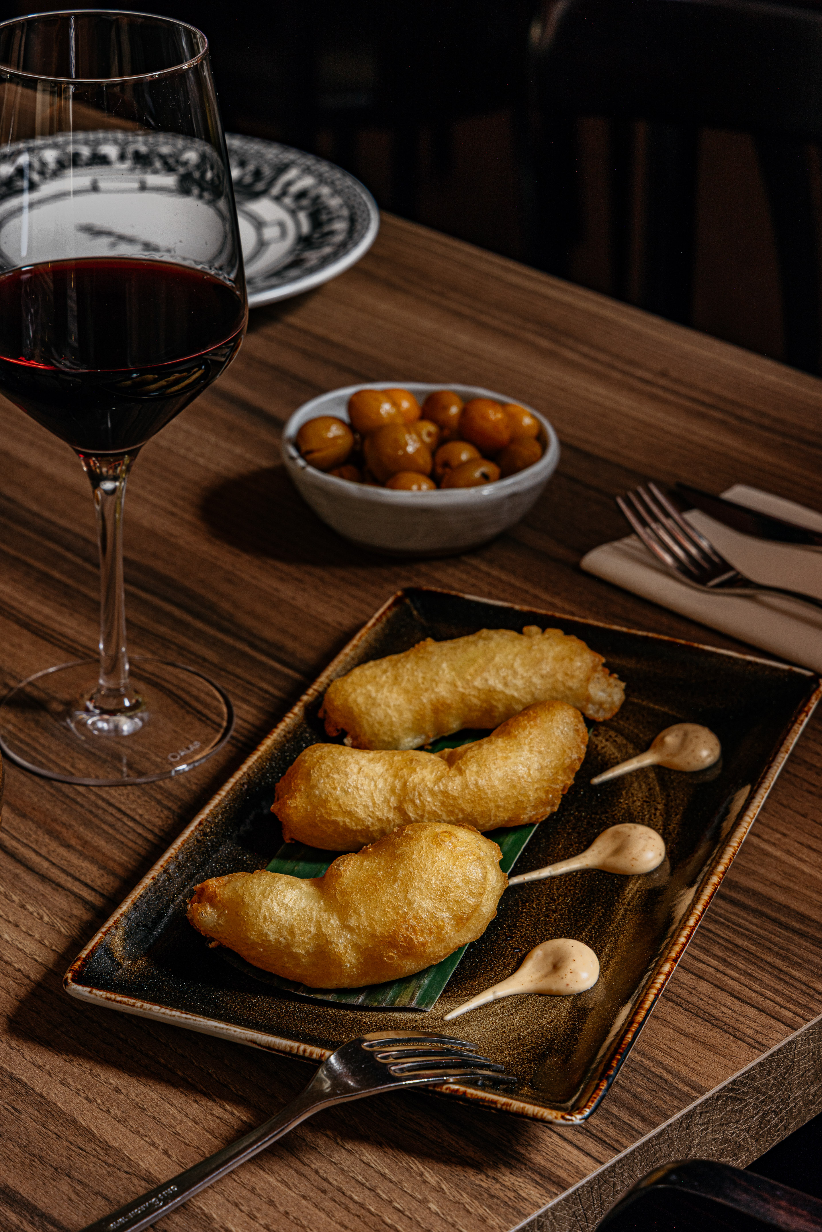 Aperitivo frito con salsa, vino tinto y aceitunas en mesa de madera.