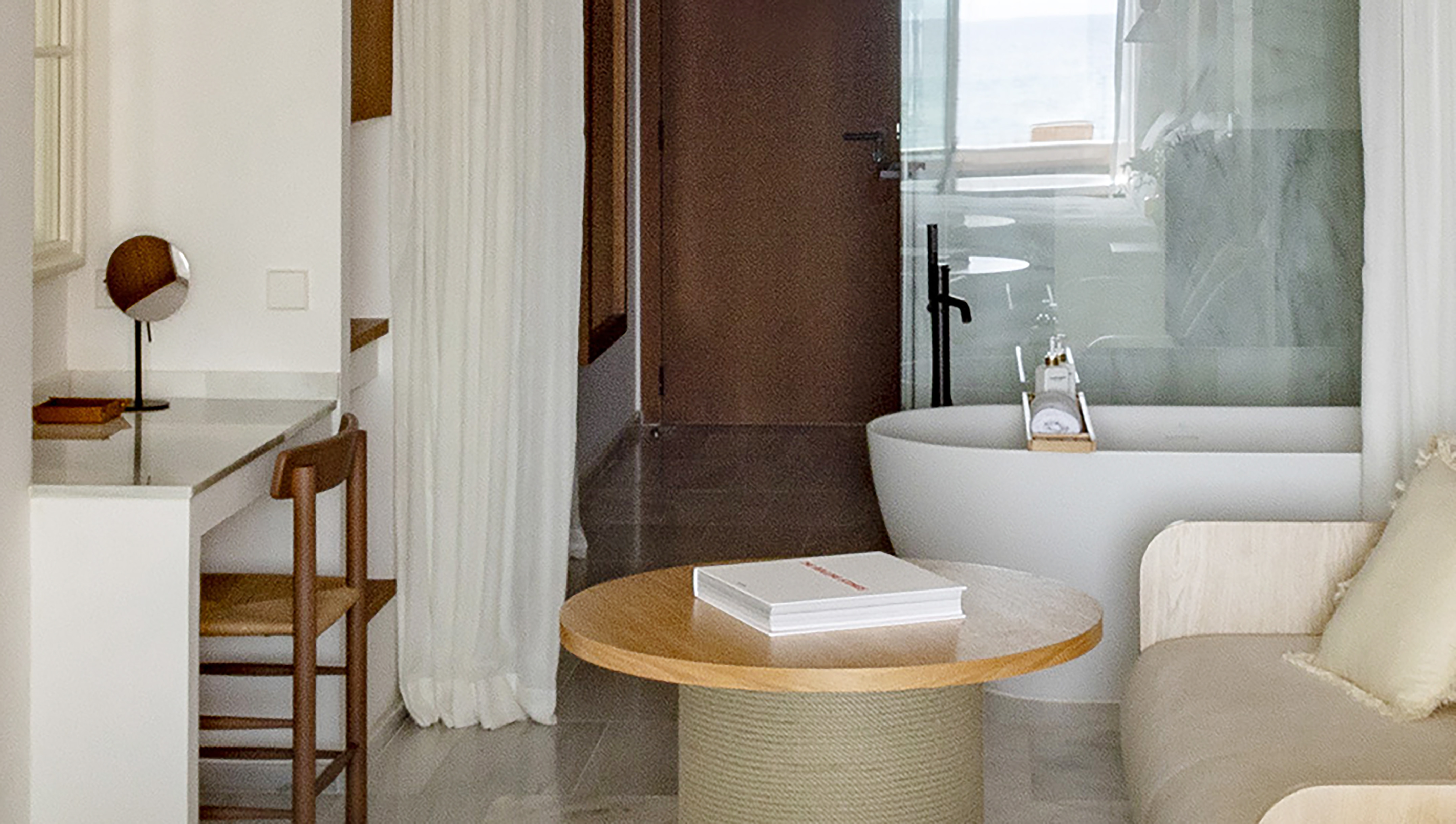 Modern hotel room with ocean view tub, vanity, and lounge area.