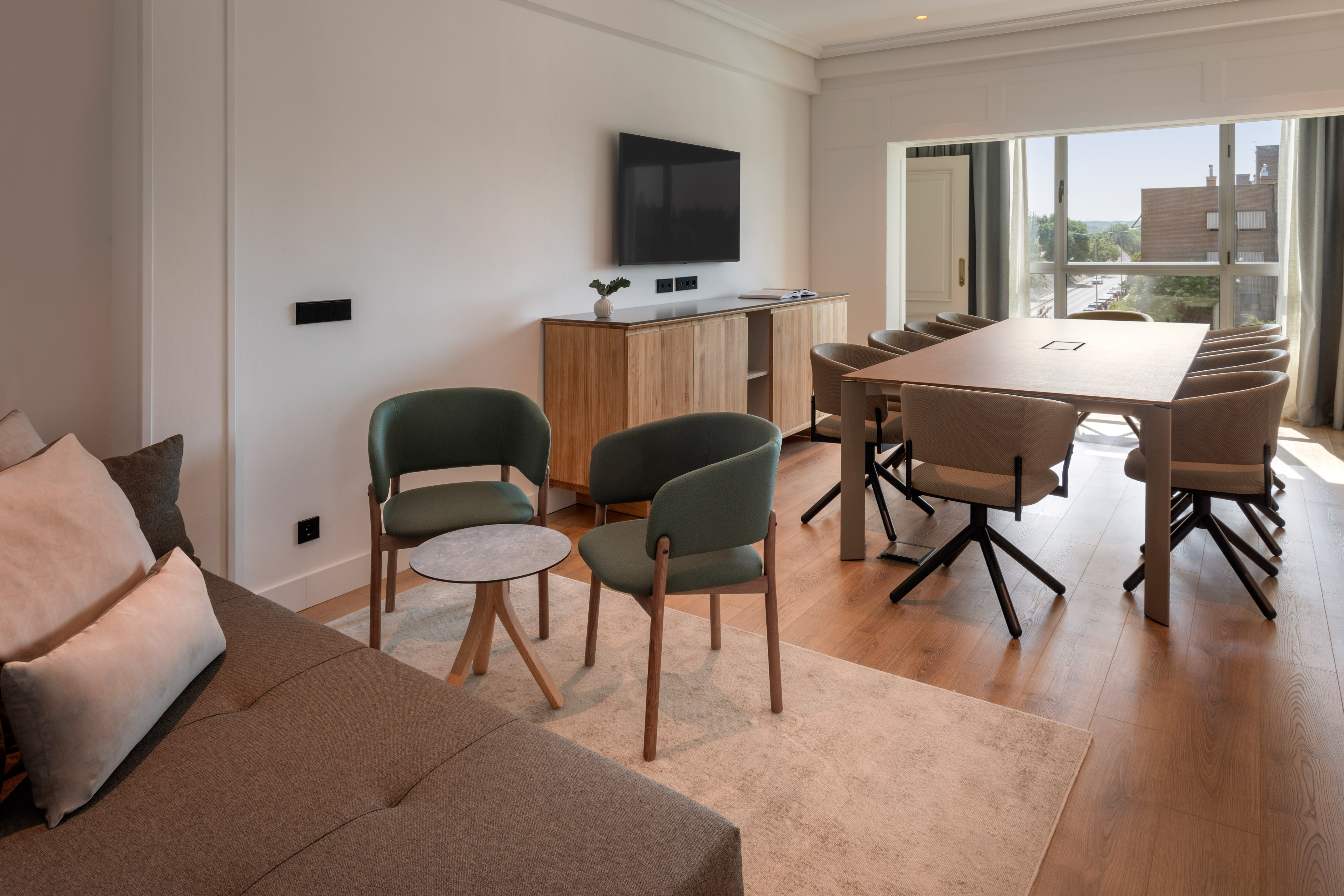 Modern suite with sofa, green armchairs, conference table, and TV.