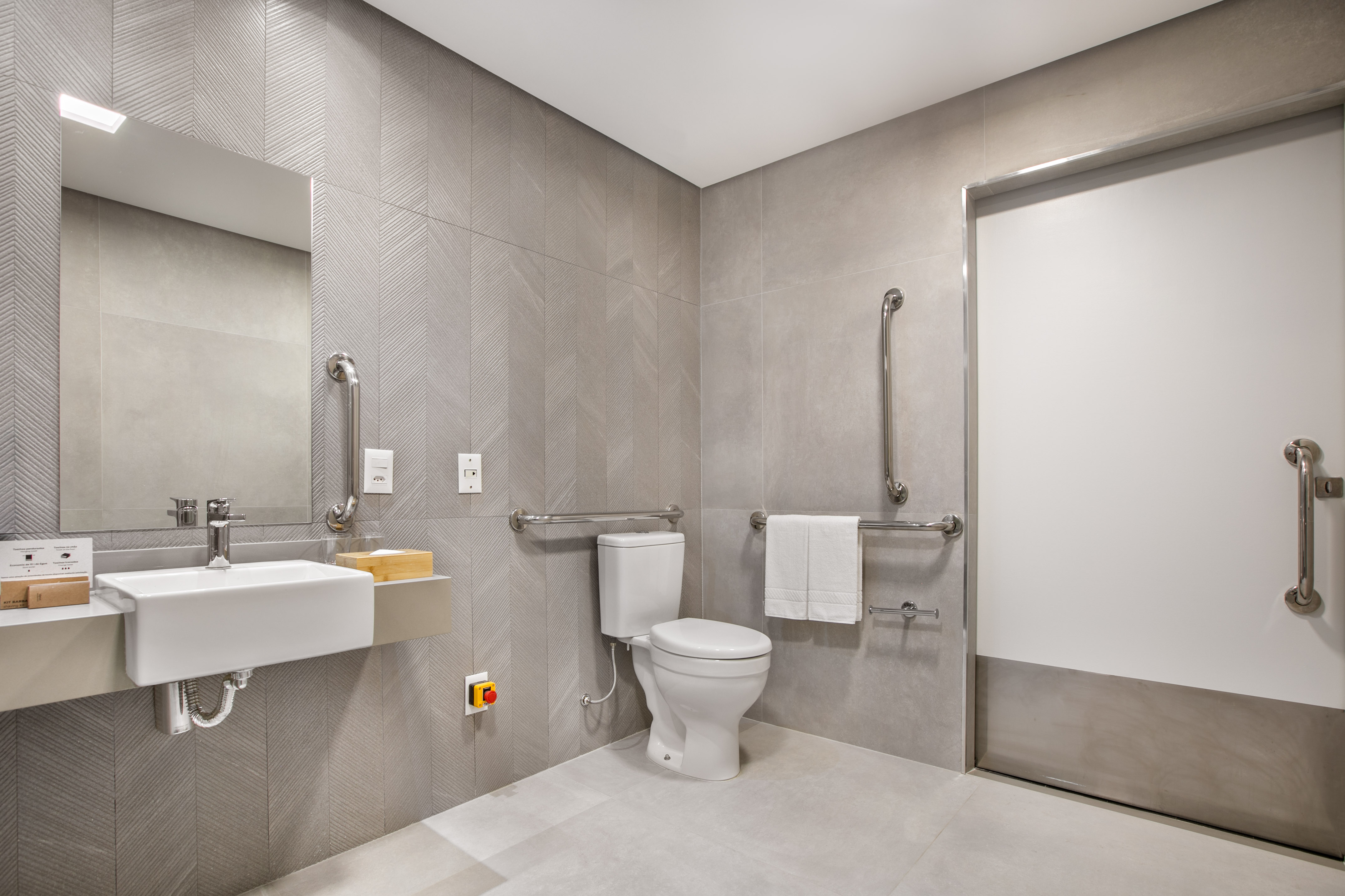 Accessible modern restroom with gray chevron tiles, grab bars, toilet, sink.