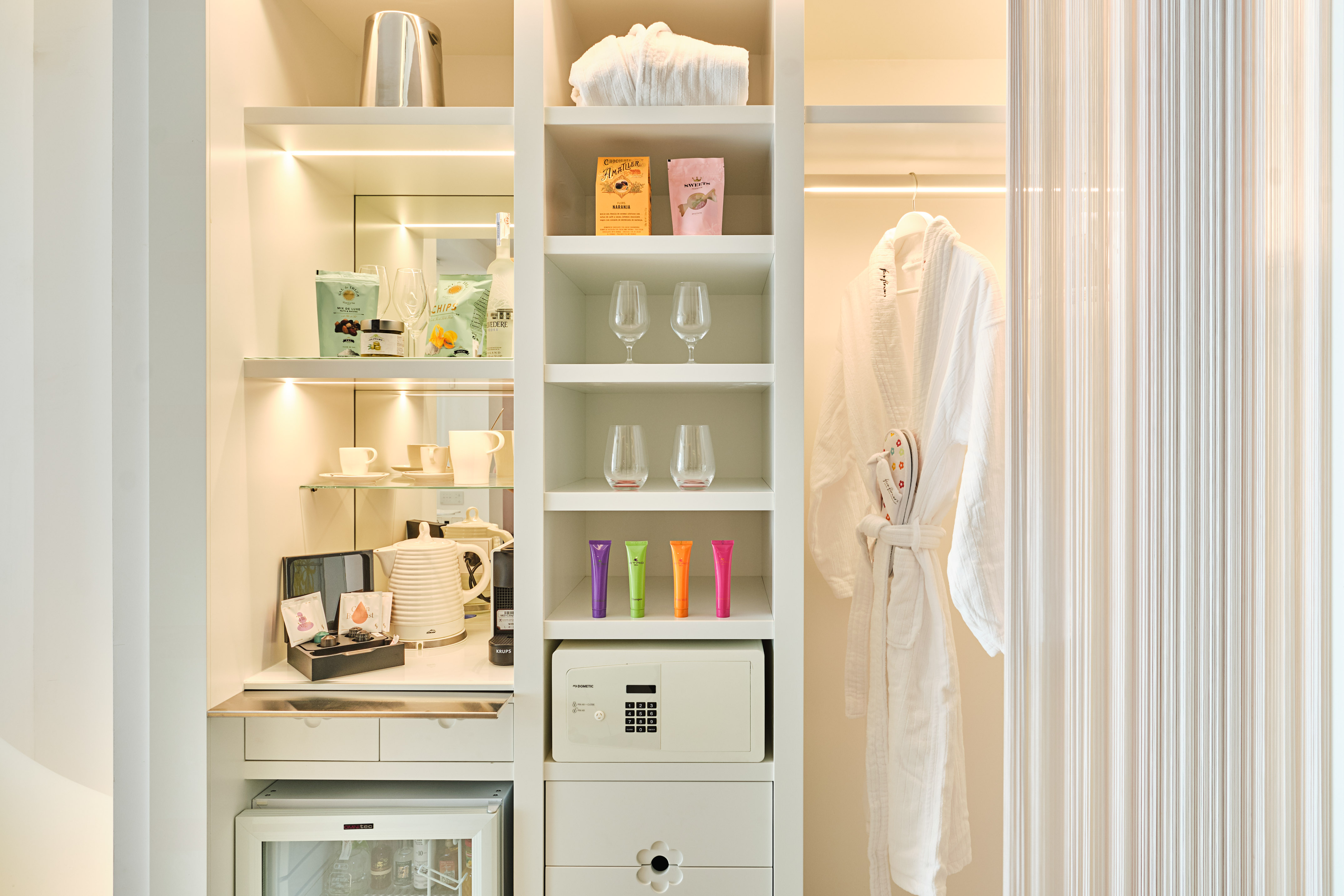 Bright hotel closet featuring minibar, coffee station, safe, and white bathrobe.