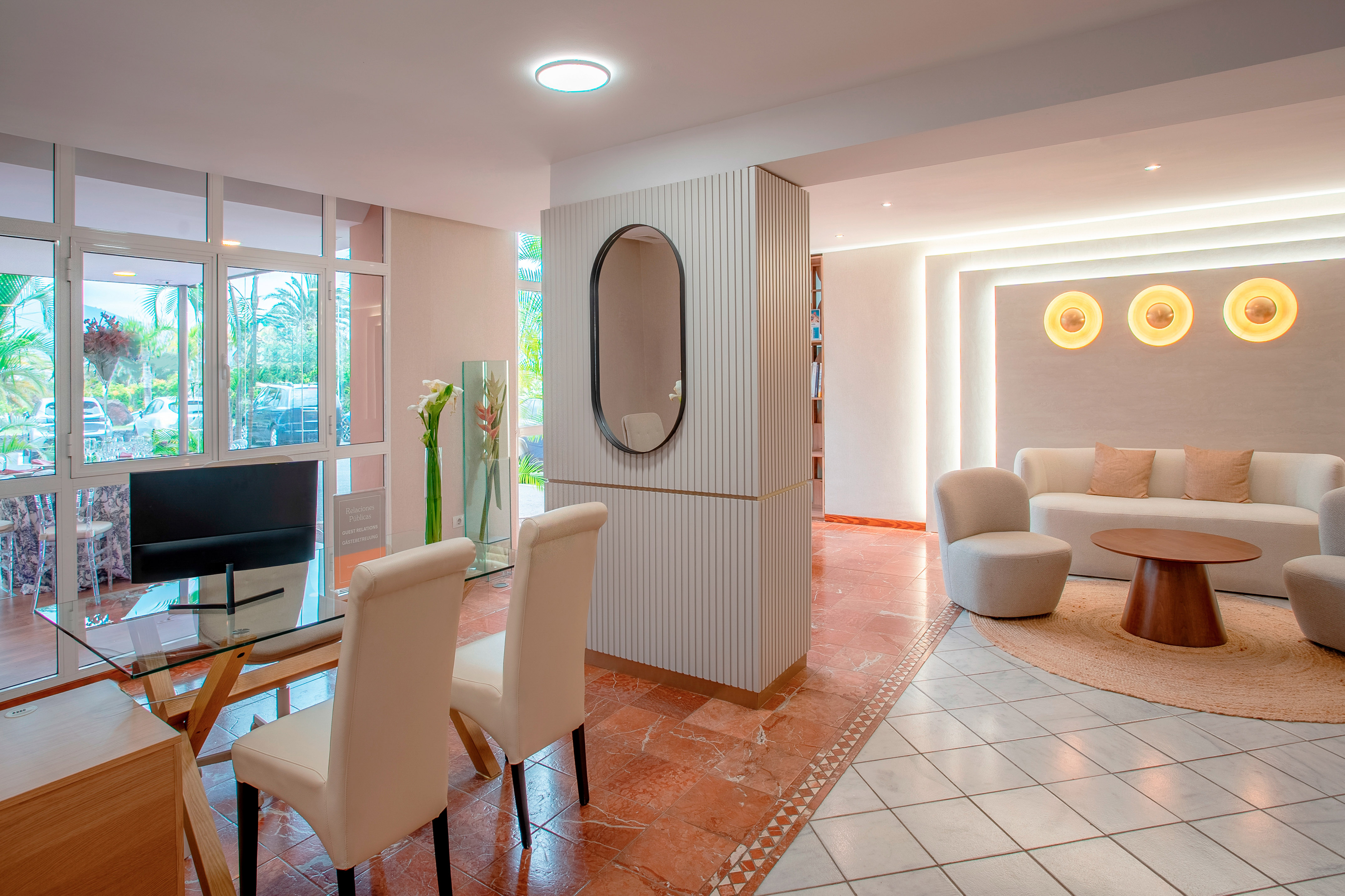 Modern hotel lobby lounge with comfortable seating, glass table, and tropical view.