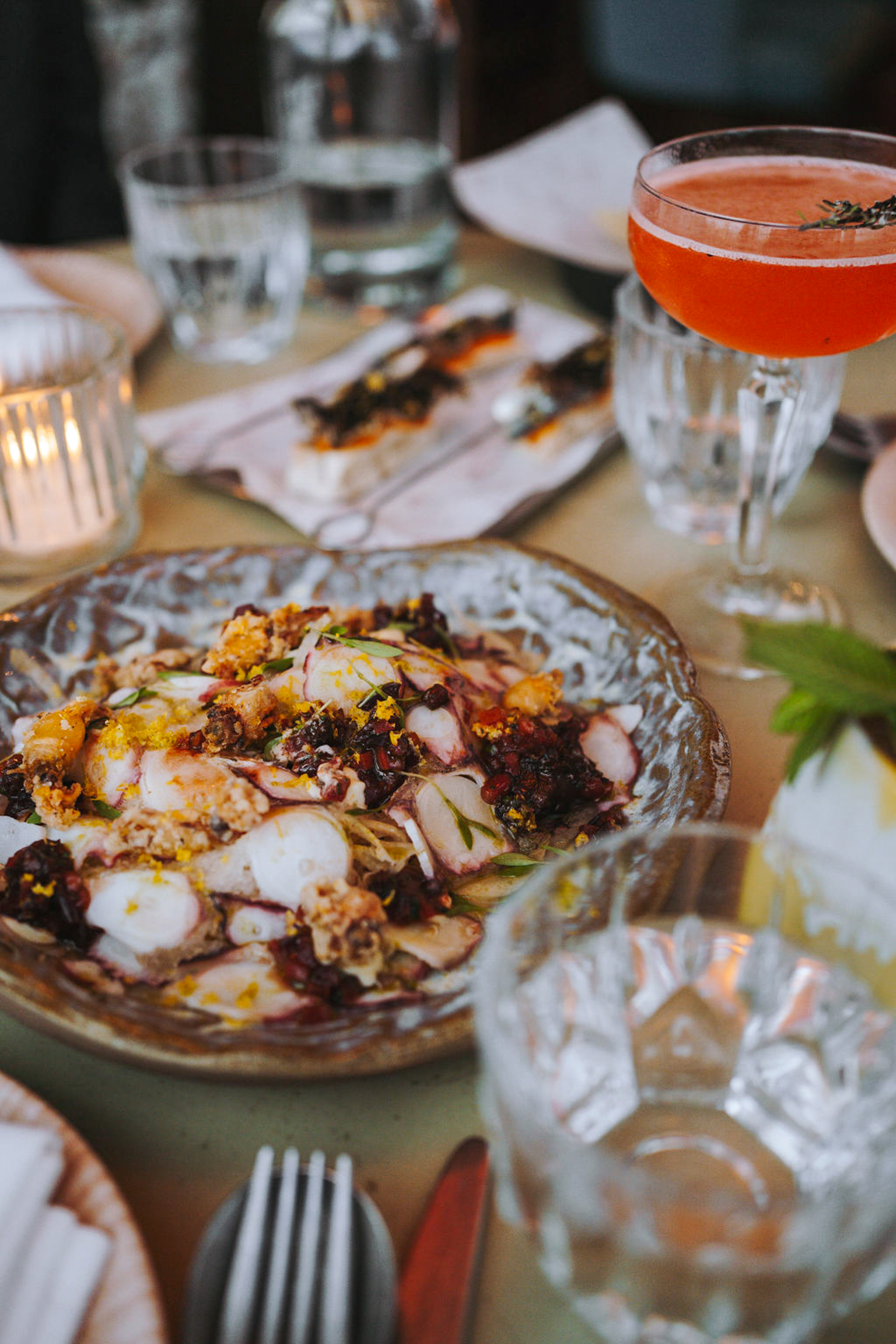 Octopus salad with crispy toppings, red cocktail, and appetizers on a dining table.