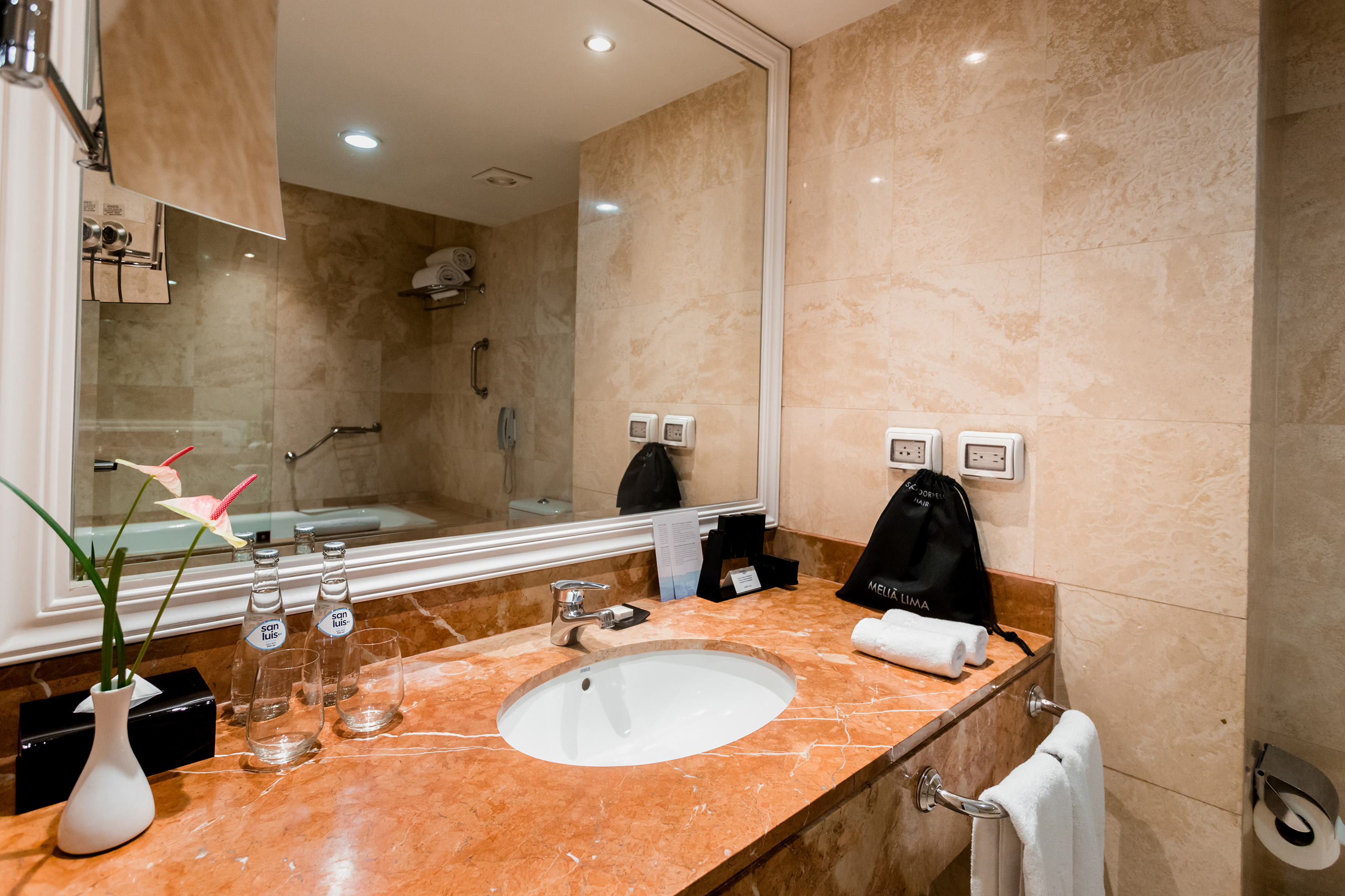 Meliá Lima hotel bathroom, red marble vanity, white sink, large mirror.