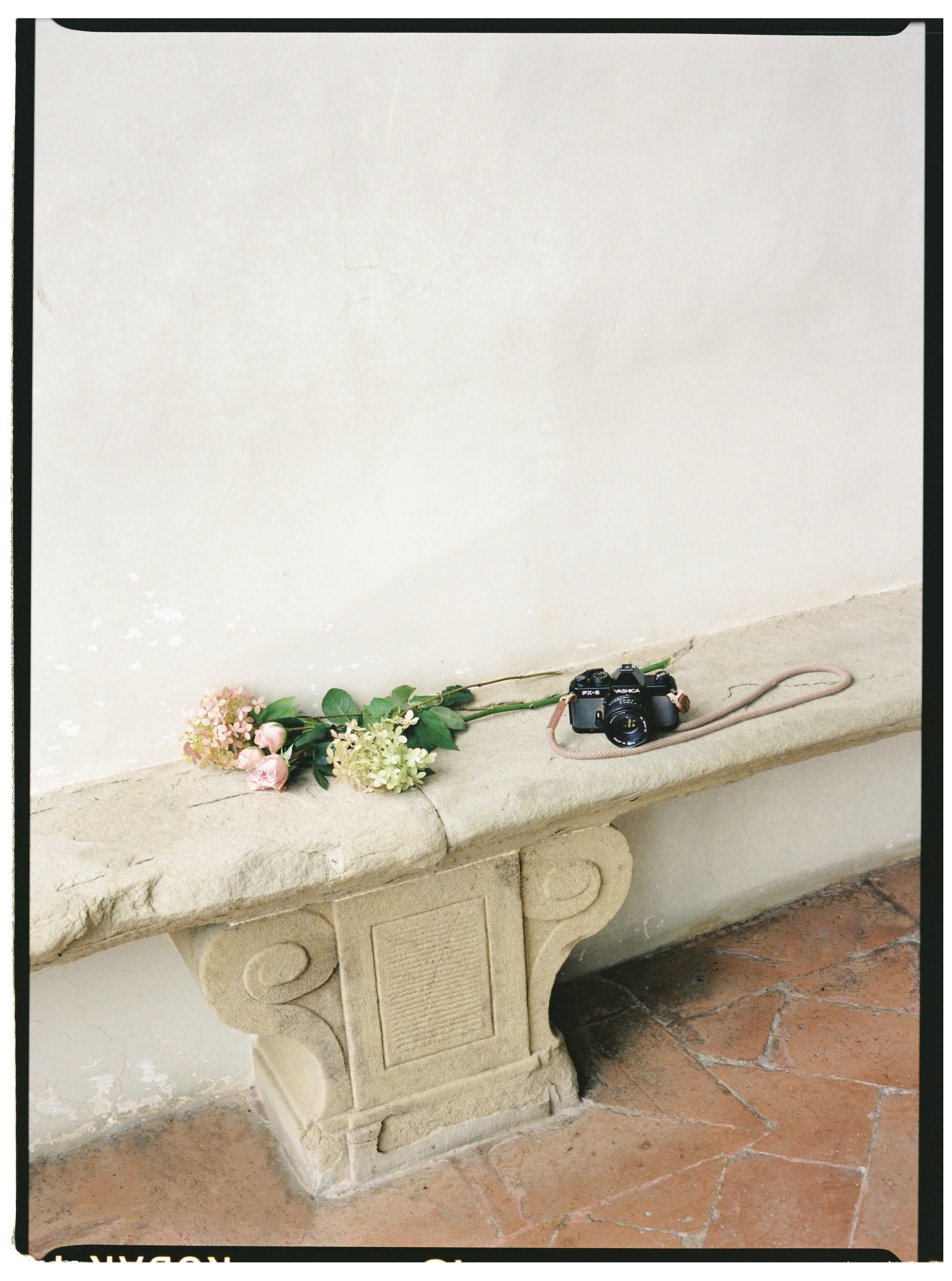 a camera and flowers on a stone bench